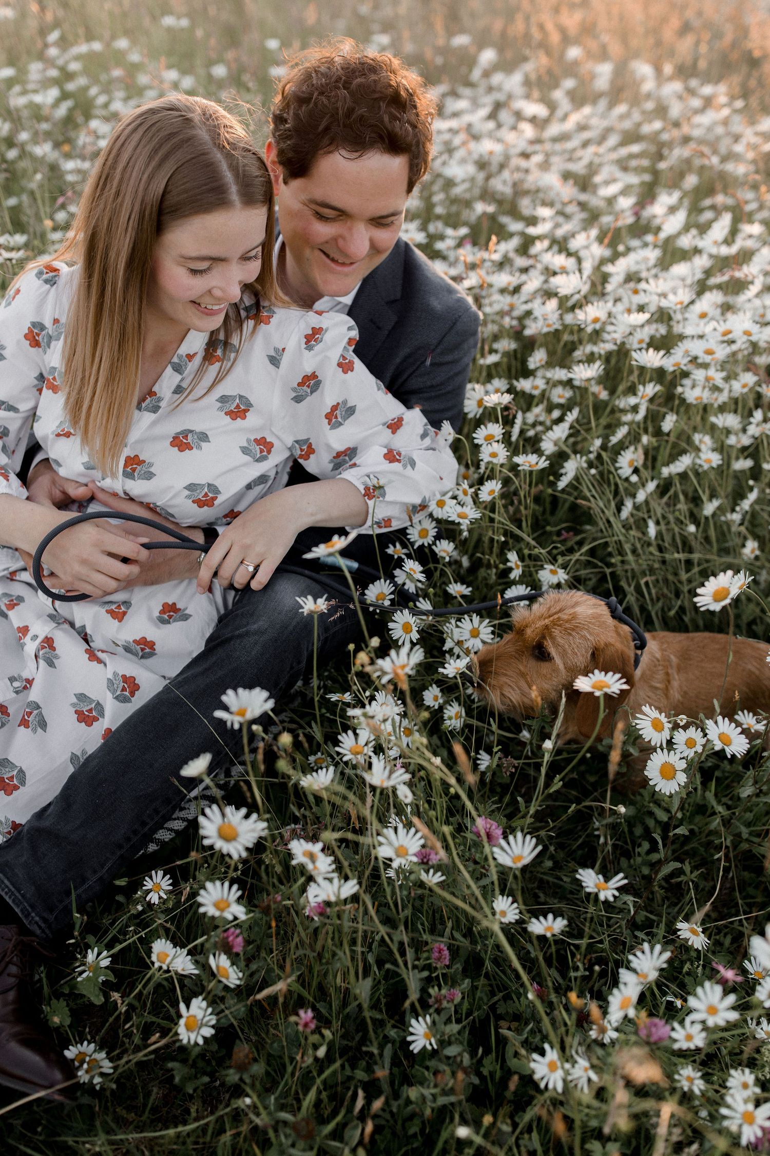 A couple sits together in a blooming daisy field during a romantic outdoor photoshoot.