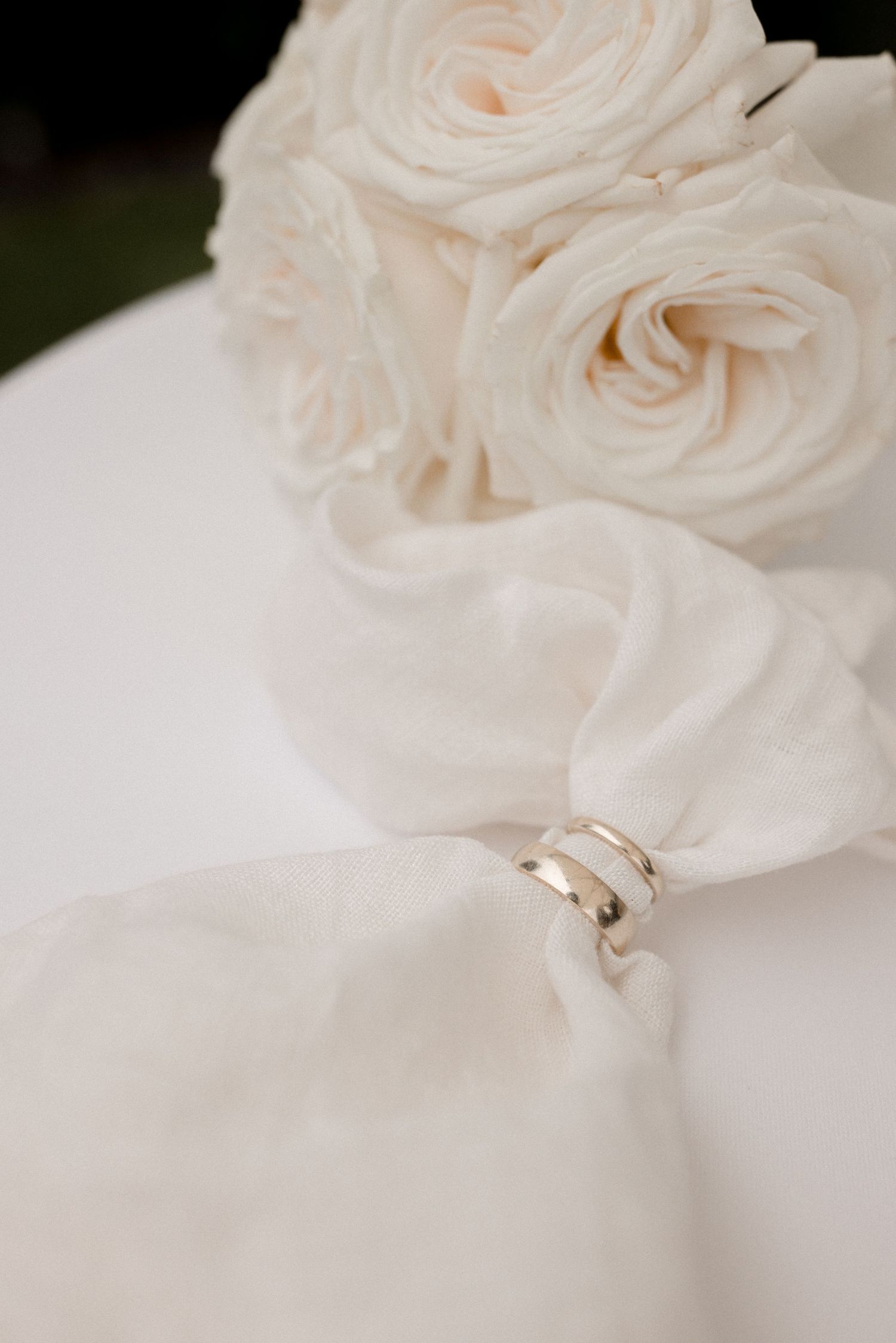 Delicate white roses and wedding rings arranged on soft white fabric at Schweizerhof Villa Luzern.