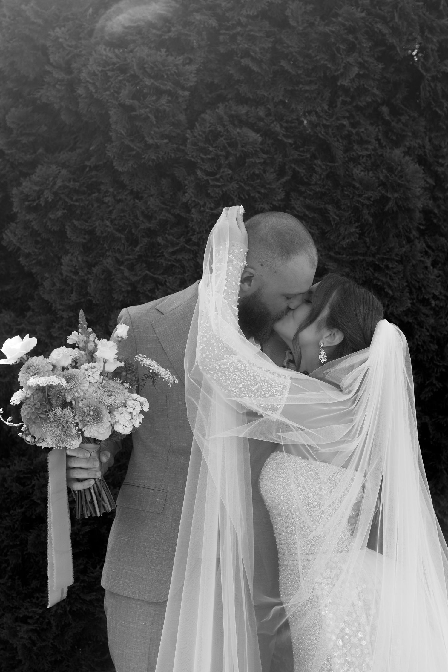 An intimate black and white portrait of newlyweds sharing a kiss beneath a long veil.