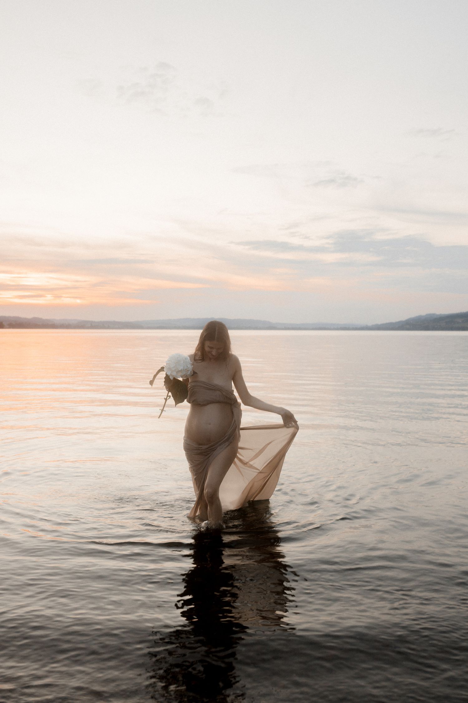 Silhouette of pregnant woman standing in lake water during golden sunset.