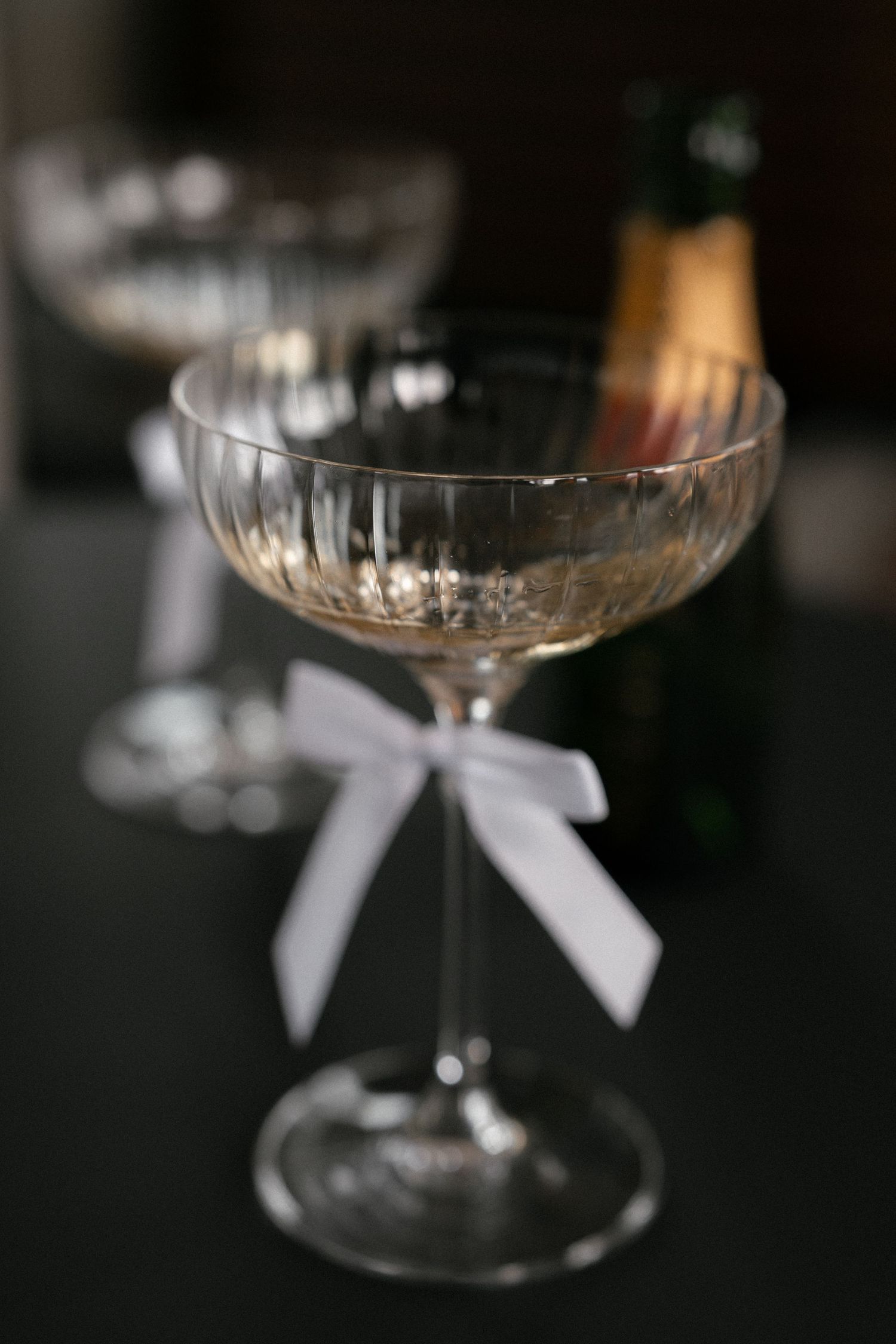 Crystal champagne coupe glasses decorated with delicate white bows.