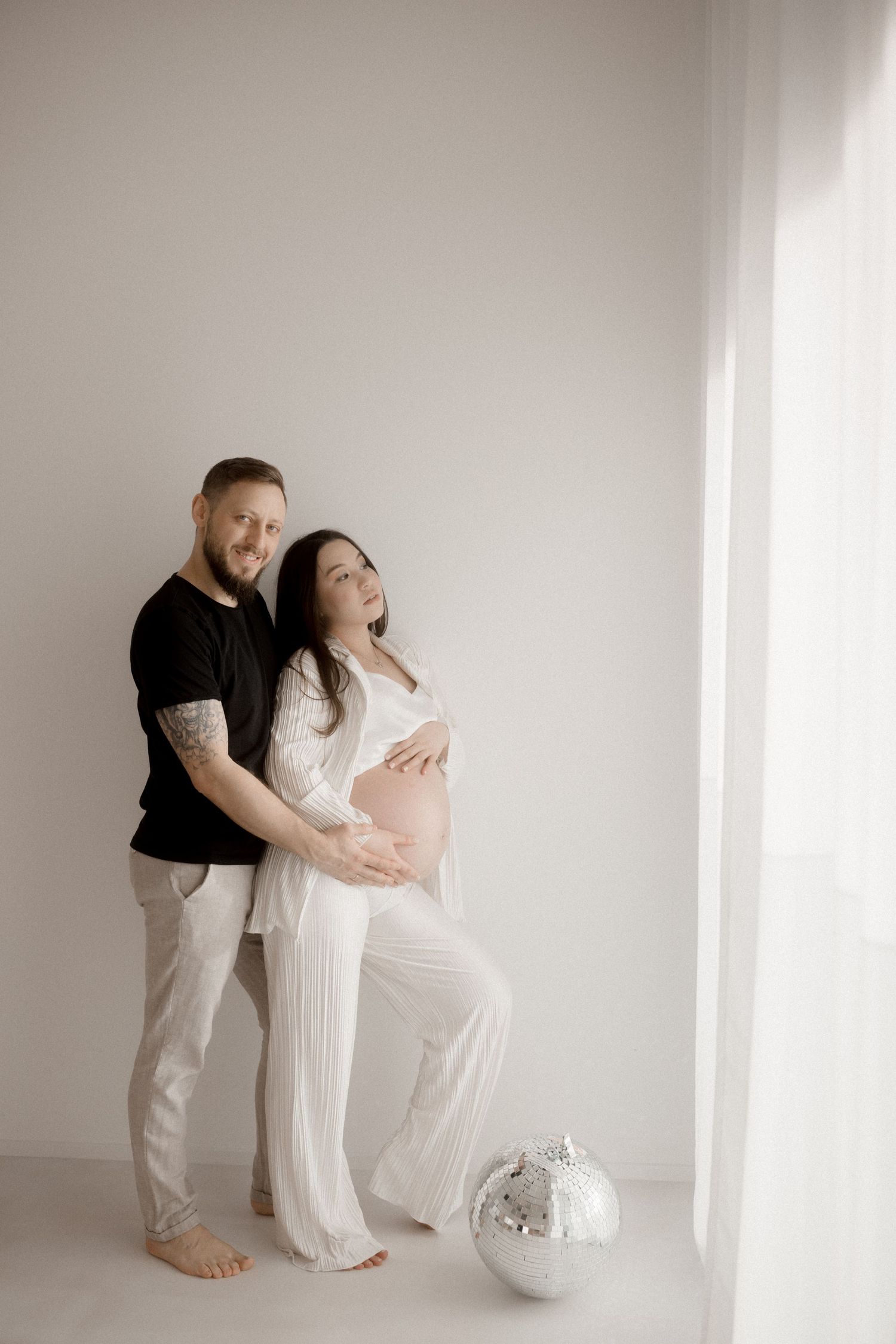 A tender maternity photoshoot in a bright white studio showing intimate moments between a couple.