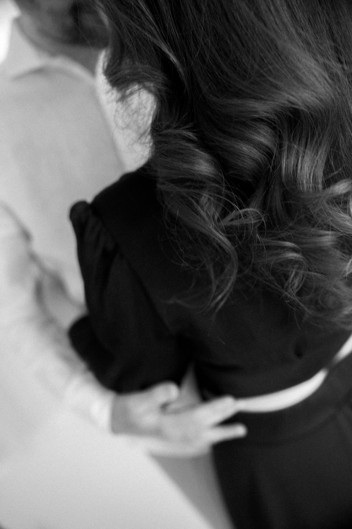 Black and white close-up portrait showing dark wavy hair against a light background.