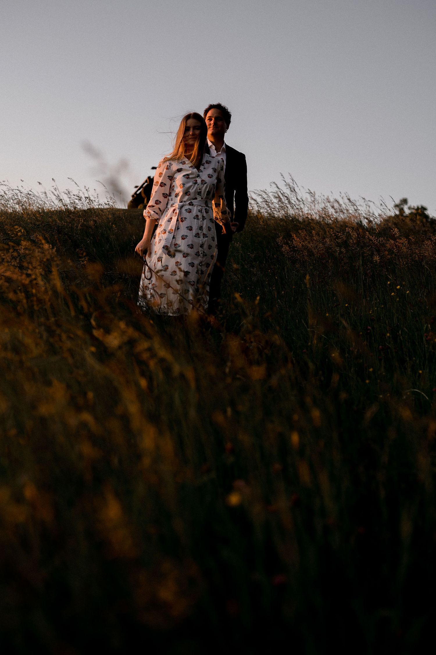 A figure in a polka dot dress stands against a dark silhouetted field at sunset.