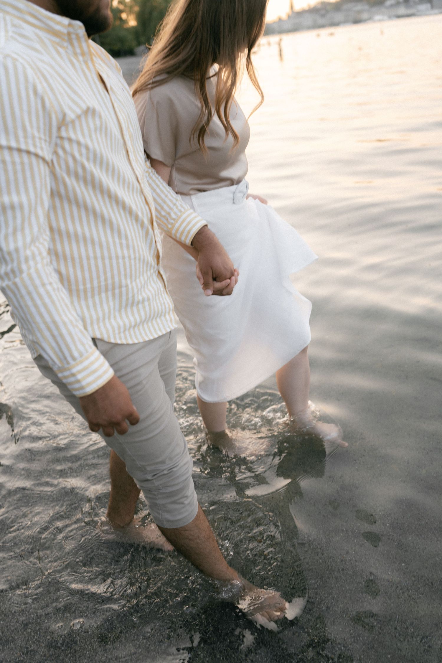 A series of close-up shots showing bare feet walking on a sandy beach in white linen clothing.