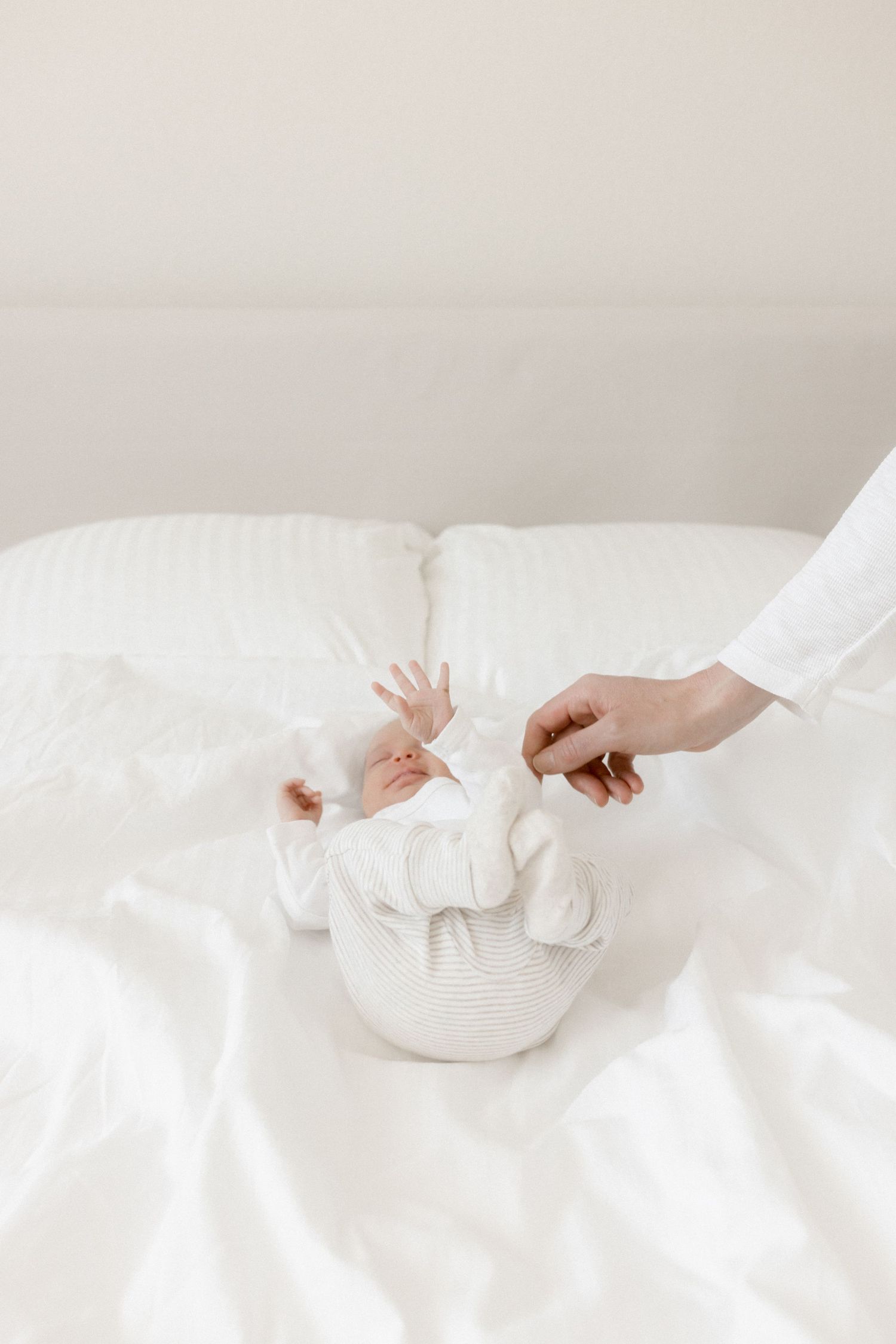 Close-up of tiny hands reaching out from soft white bedding and blankets.