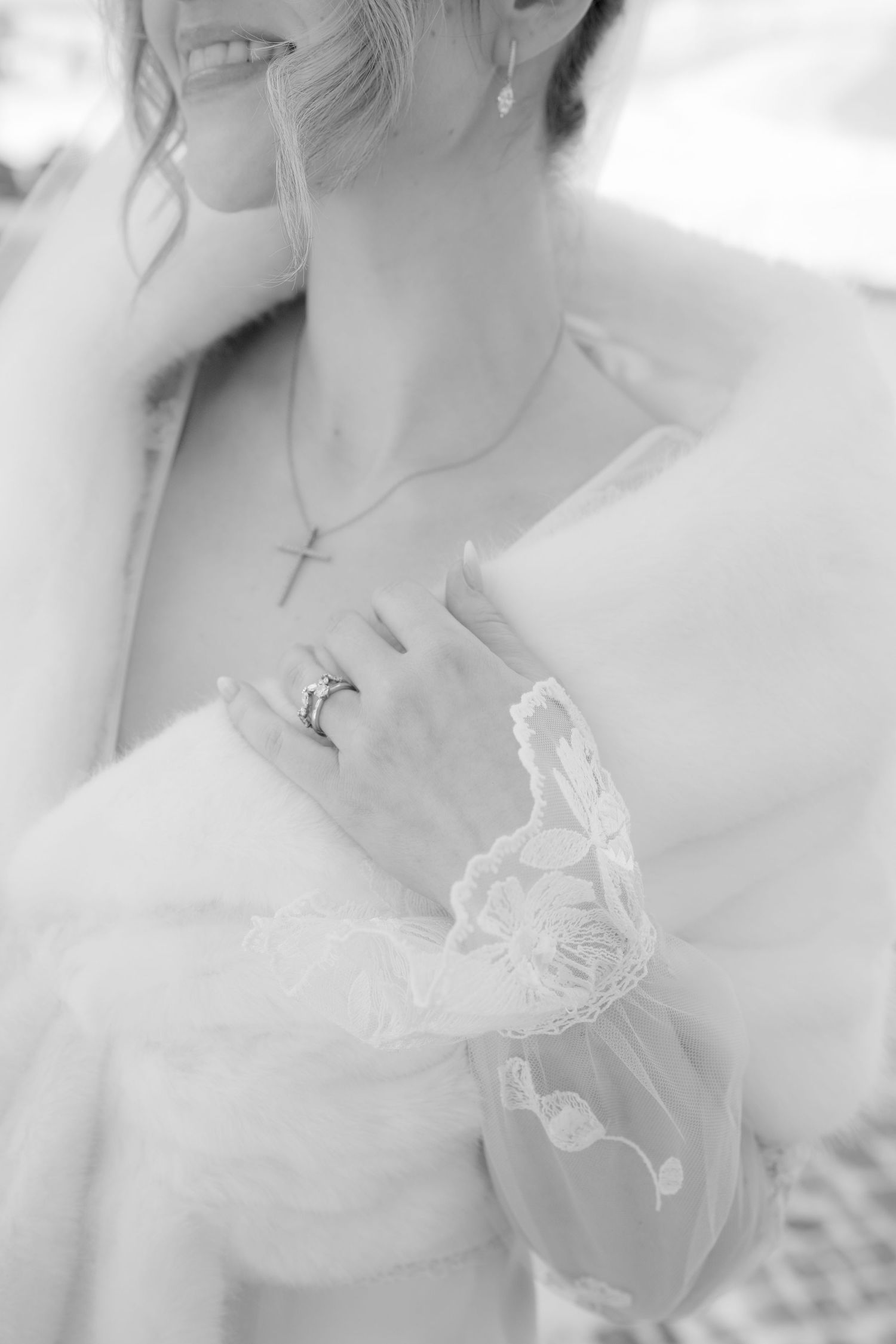 Black and white bridal photo showcasing a cross necklace, diamond ring, and delicate lace wedding dress details.