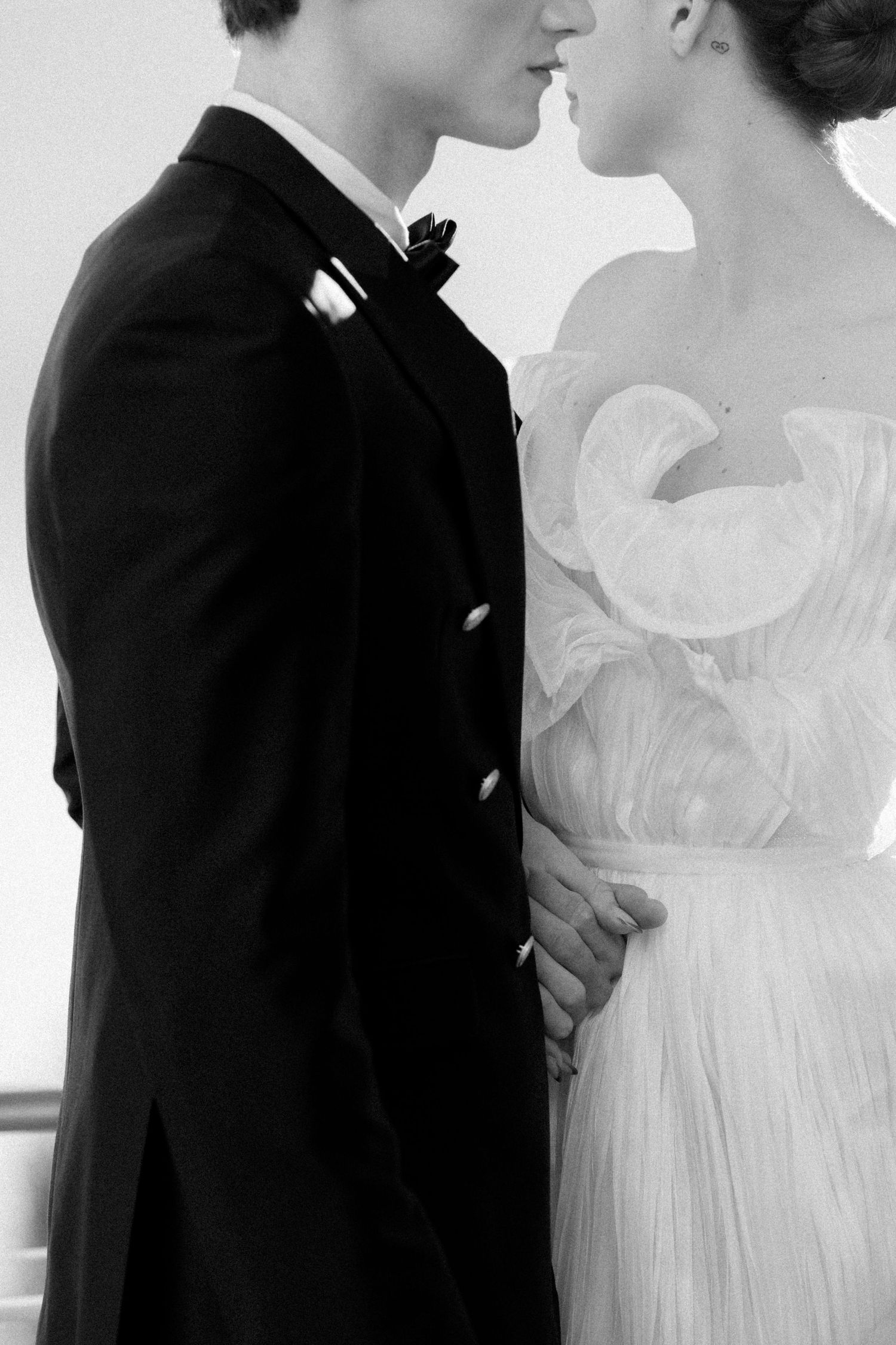 Black and white photo of a couple in wedding attire, groom in tuxedo and bride in white gown, sharing an intimate moment.