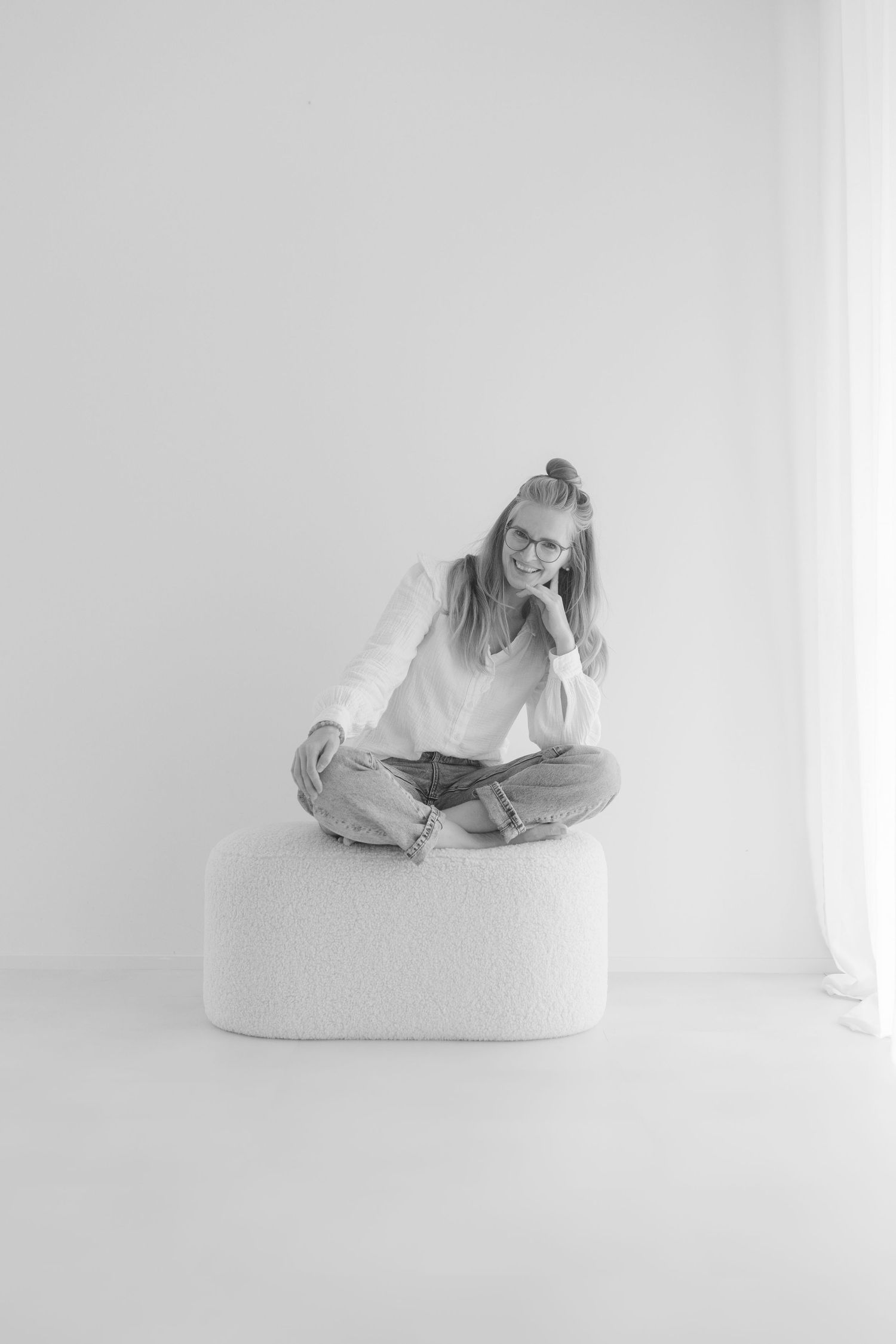 Figure reclining on white cushions in minimalist studio setting.