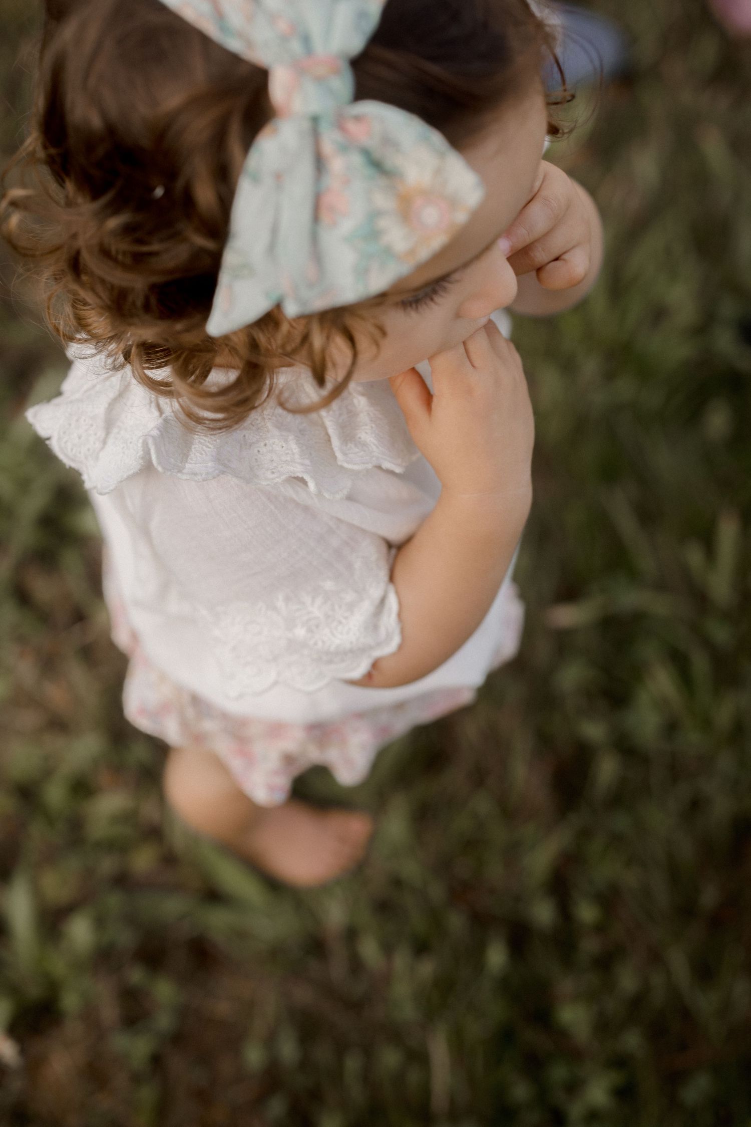 Close-up detail shot of white lace dress and floral hair bow.