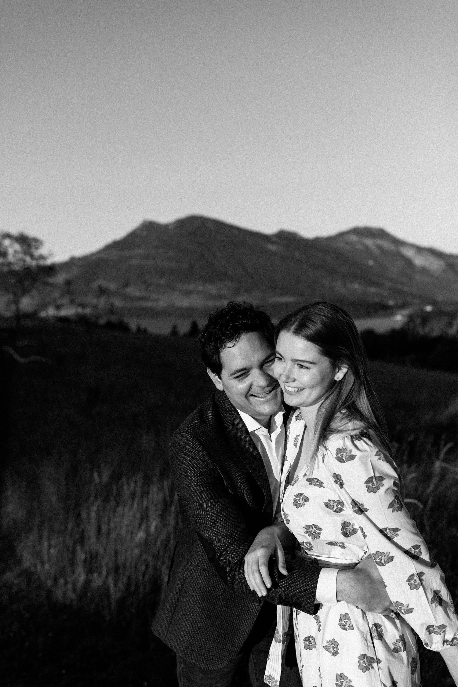 A couple shares an intimate black and white moment against a mountainous landscape backdrop.