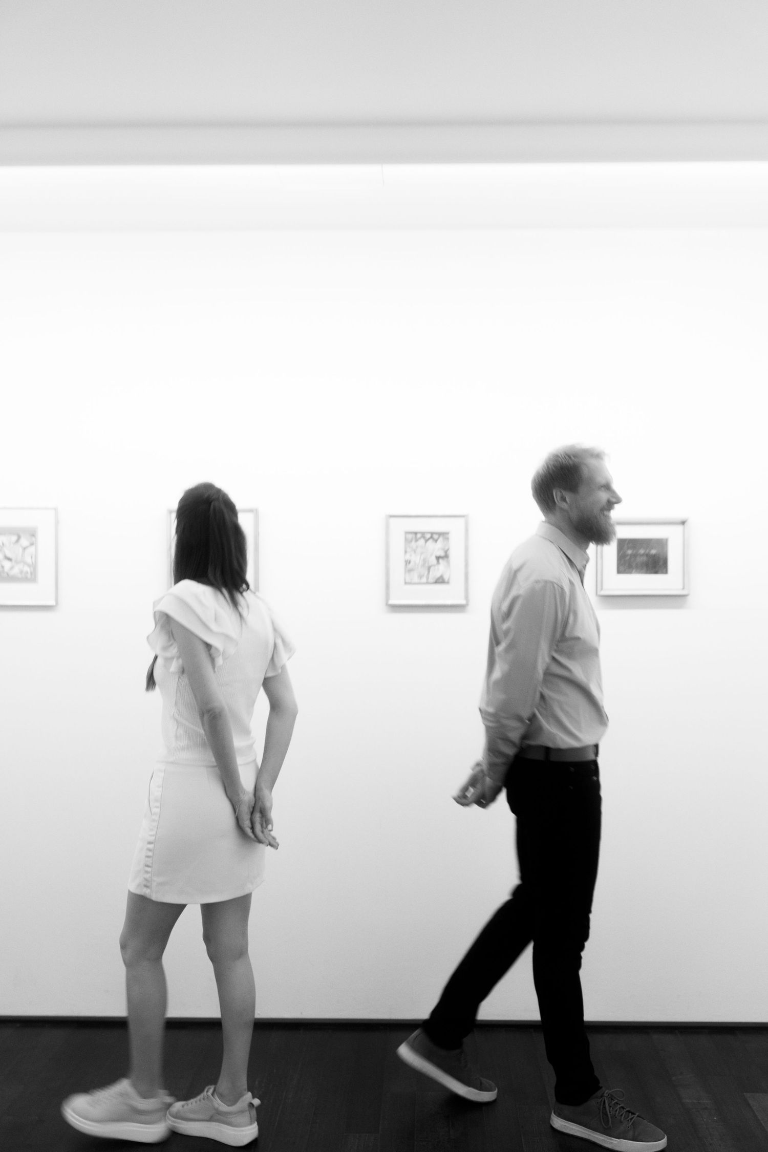 Two people walking past white gallery walls displaying artwork in a minimalist exhibition space.