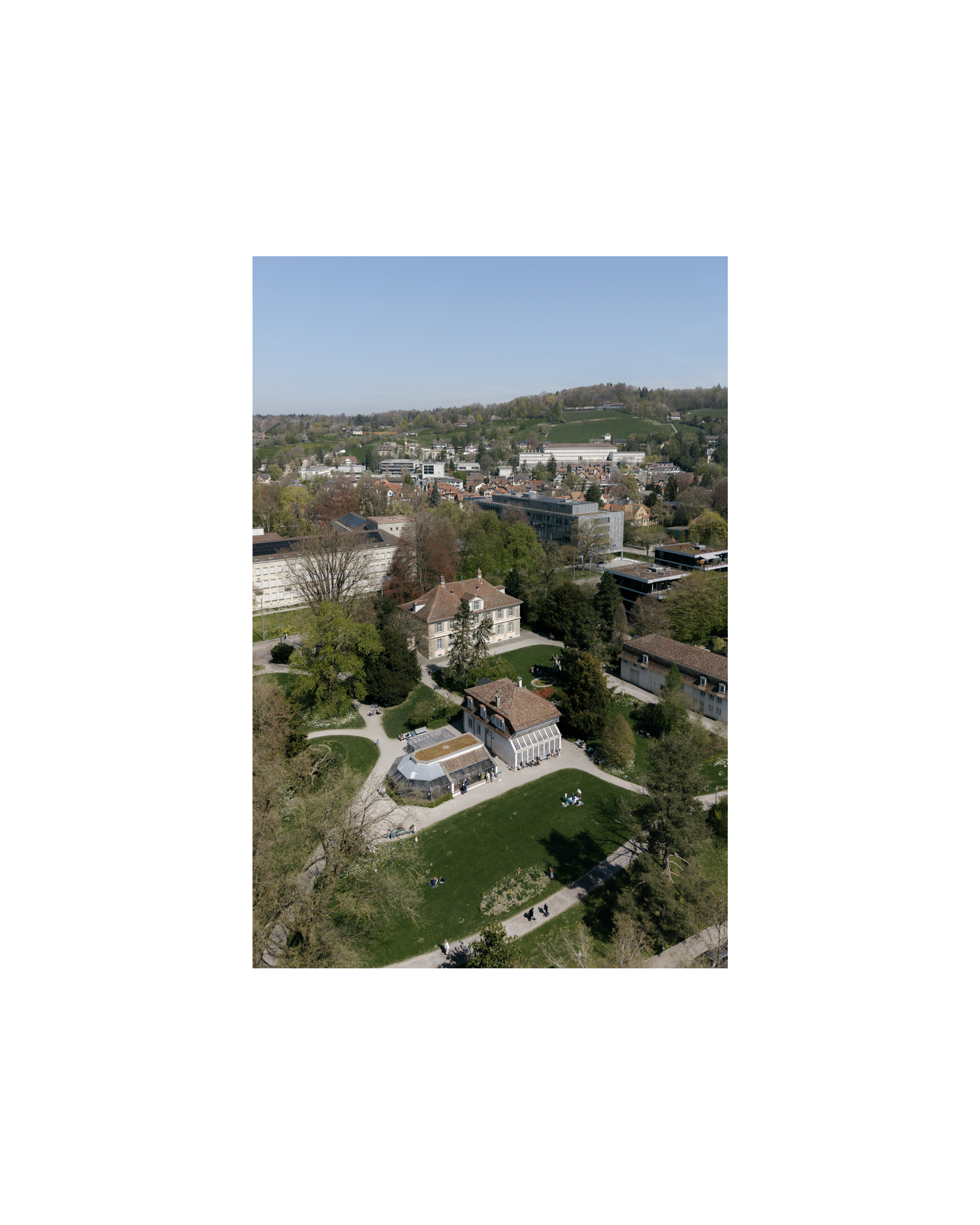 Aerial view of a European town with historic buildings, green trees, and urban landscape under a clear blue sky.