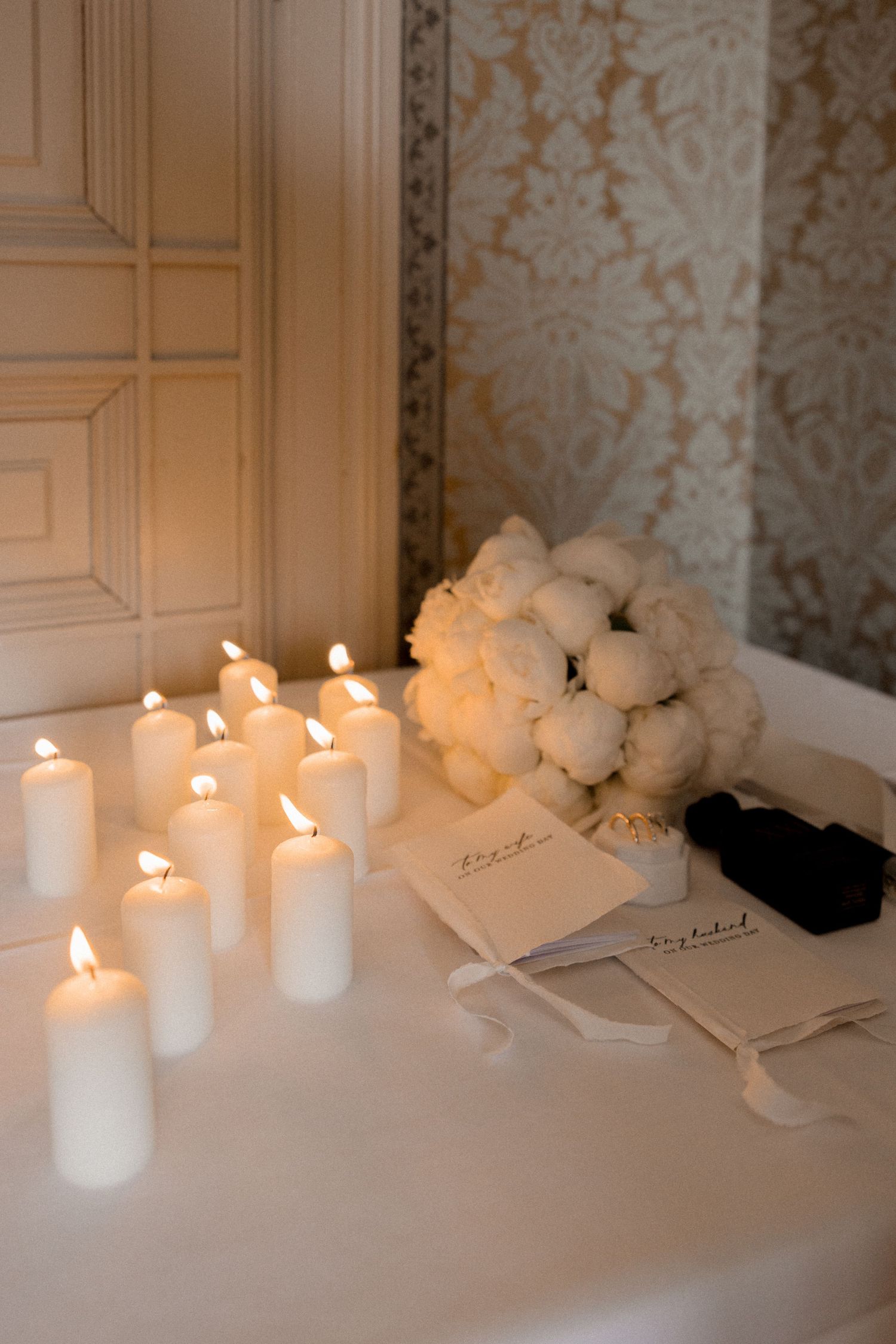 Romantic table decor with white pillar candles and roses against textured wallpaper.