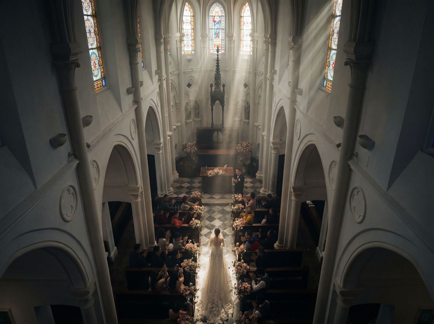 Aerial view of a bride walking down the aisle in a grand cathedral with stained glass windows and rays of light.