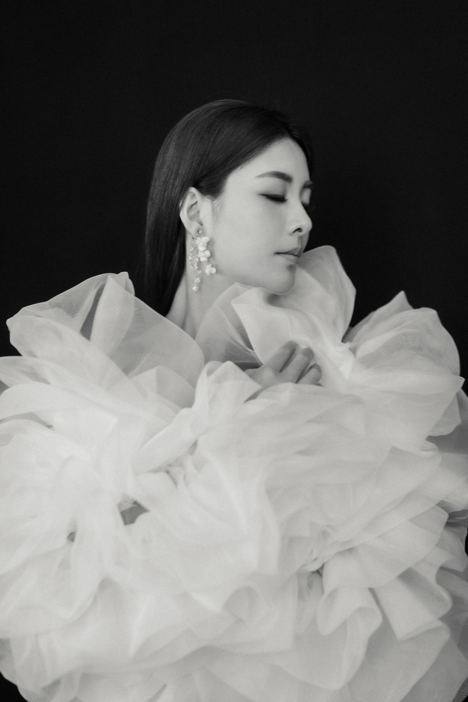 Artistic black and white portrait with ethereal white ruffled fabric against dark background.