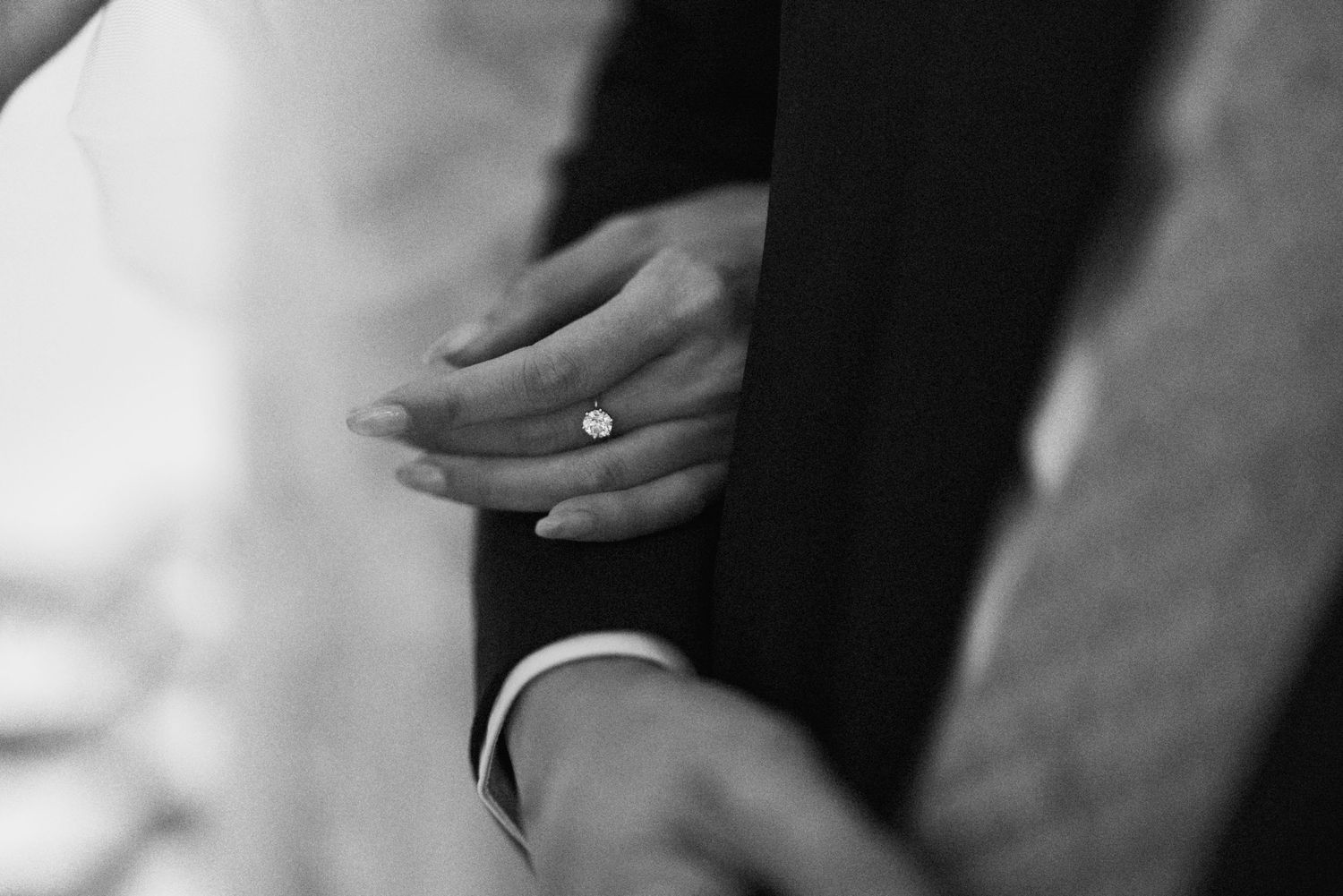 Close-up black and white photo of hands during a wedding ceremony with rings and formal attire.