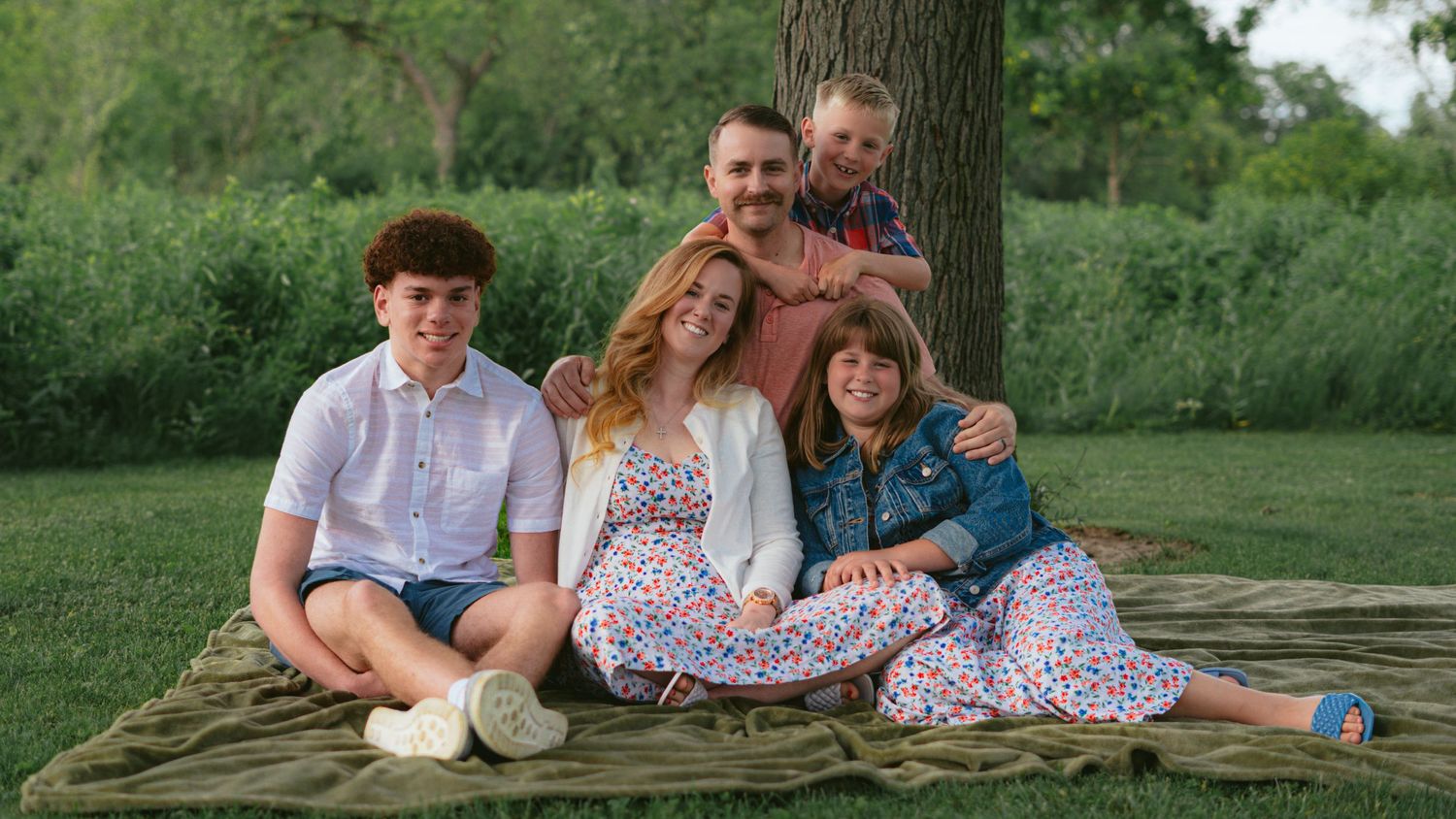 Family of five seated on a log in a green meadow, outdoor family portrait