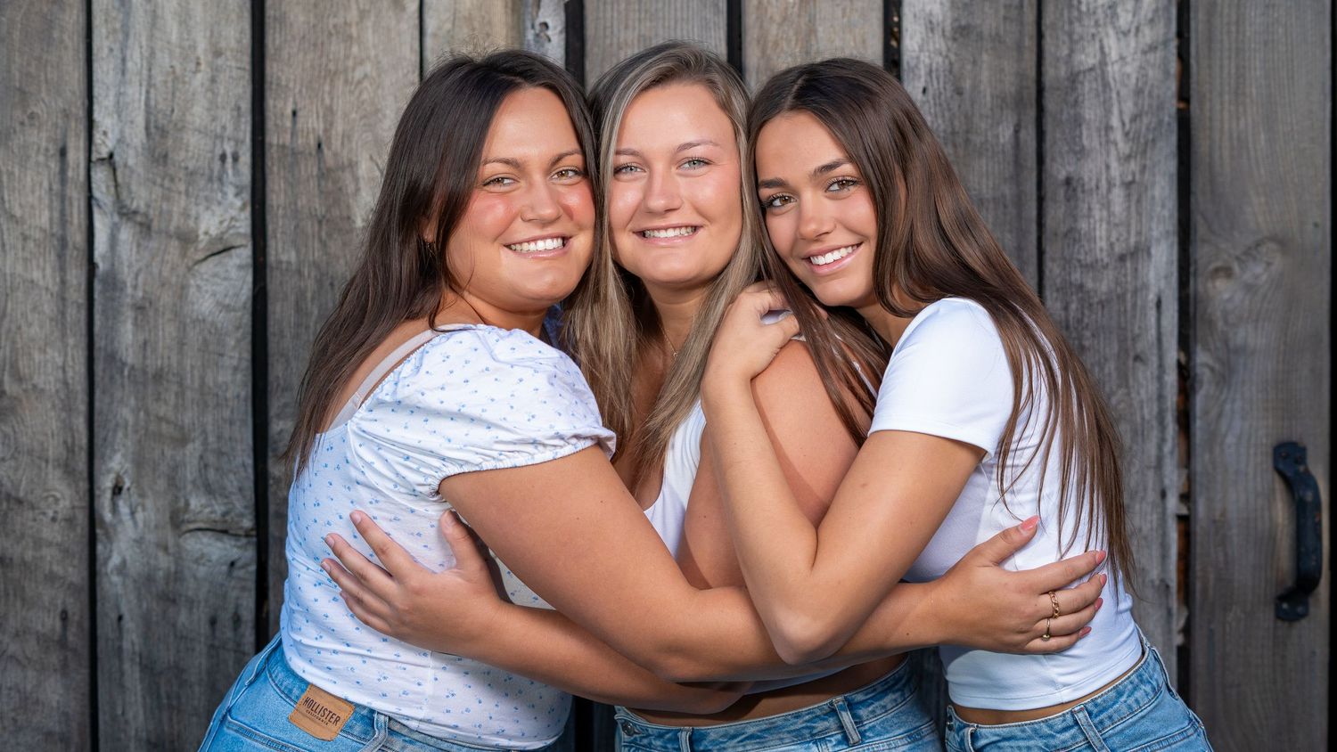 Three sisters hugging in front of a barn, candid family portrait