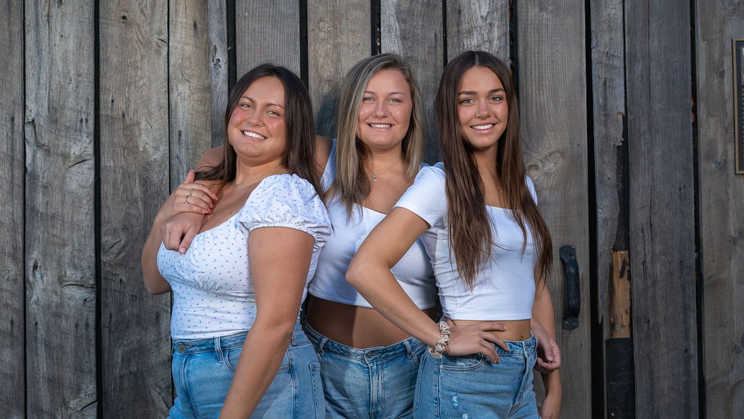 Three friends posing together against a rustic barn wall, group portrait