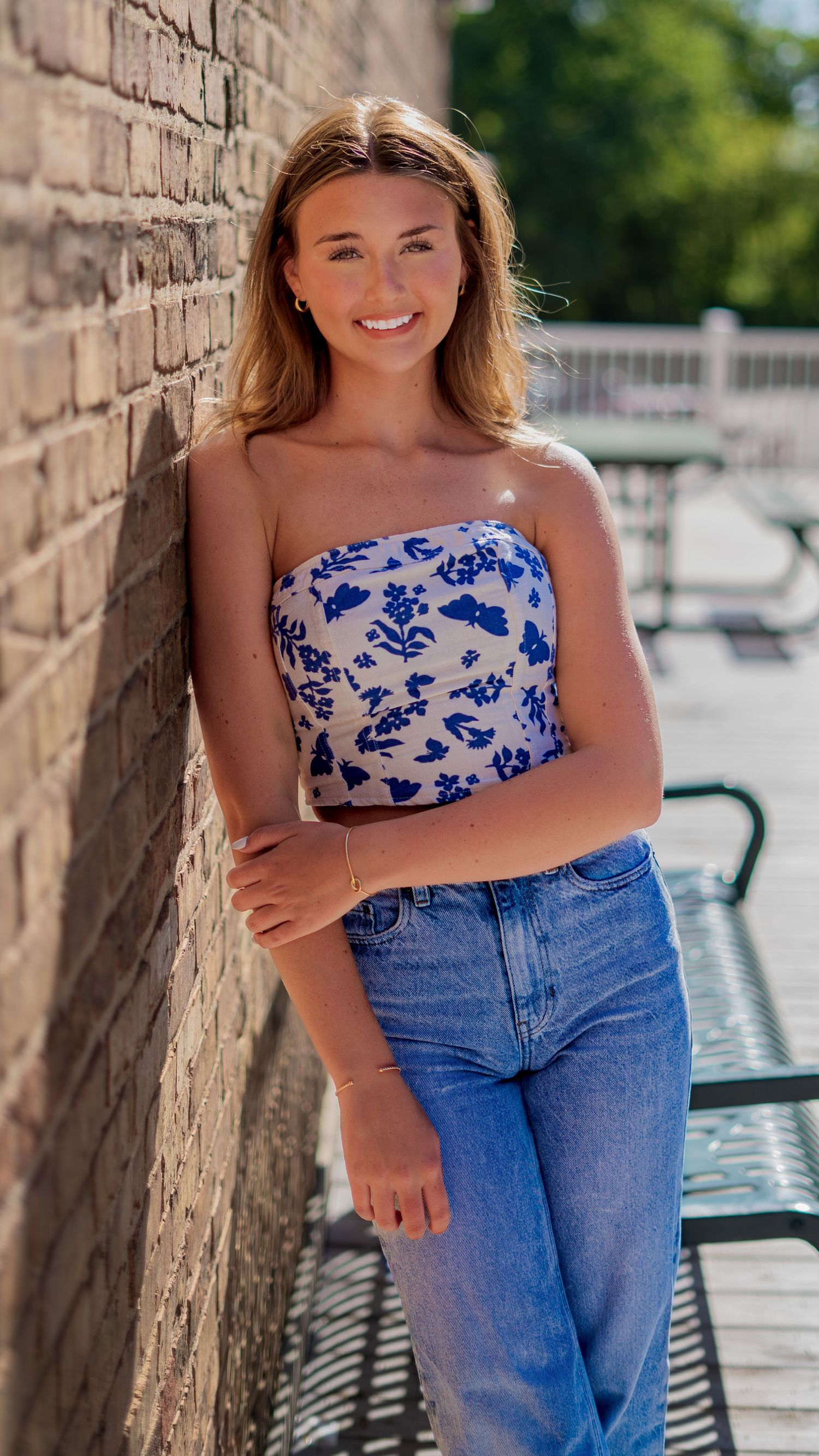 Senior portrait in a floral top and jeans by a brick wall
