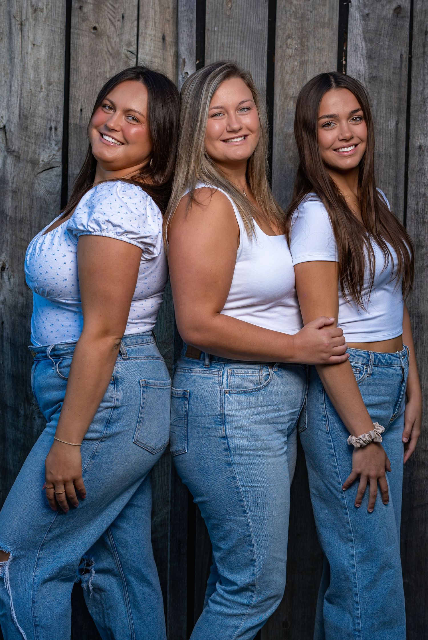 Three sisters posing together in white shirts and jeans during a portrait session.