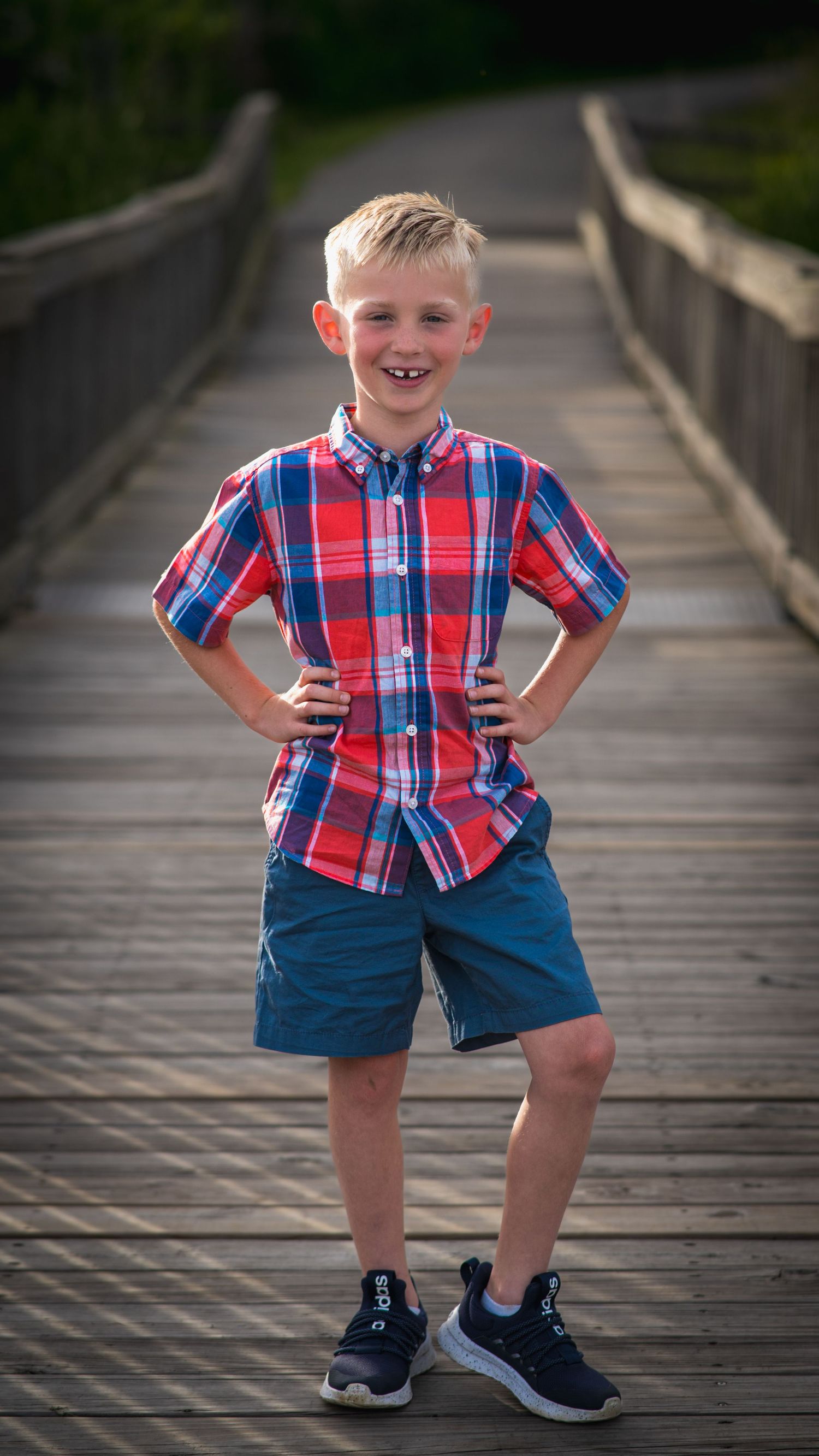 Young boy in a plaid shirt posing on a wooden bridge, family session