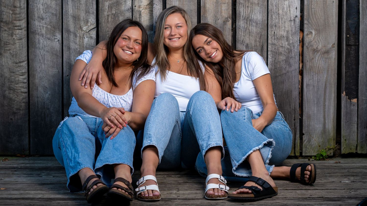 Three sisters seated together in front of a barn wall, family portrait