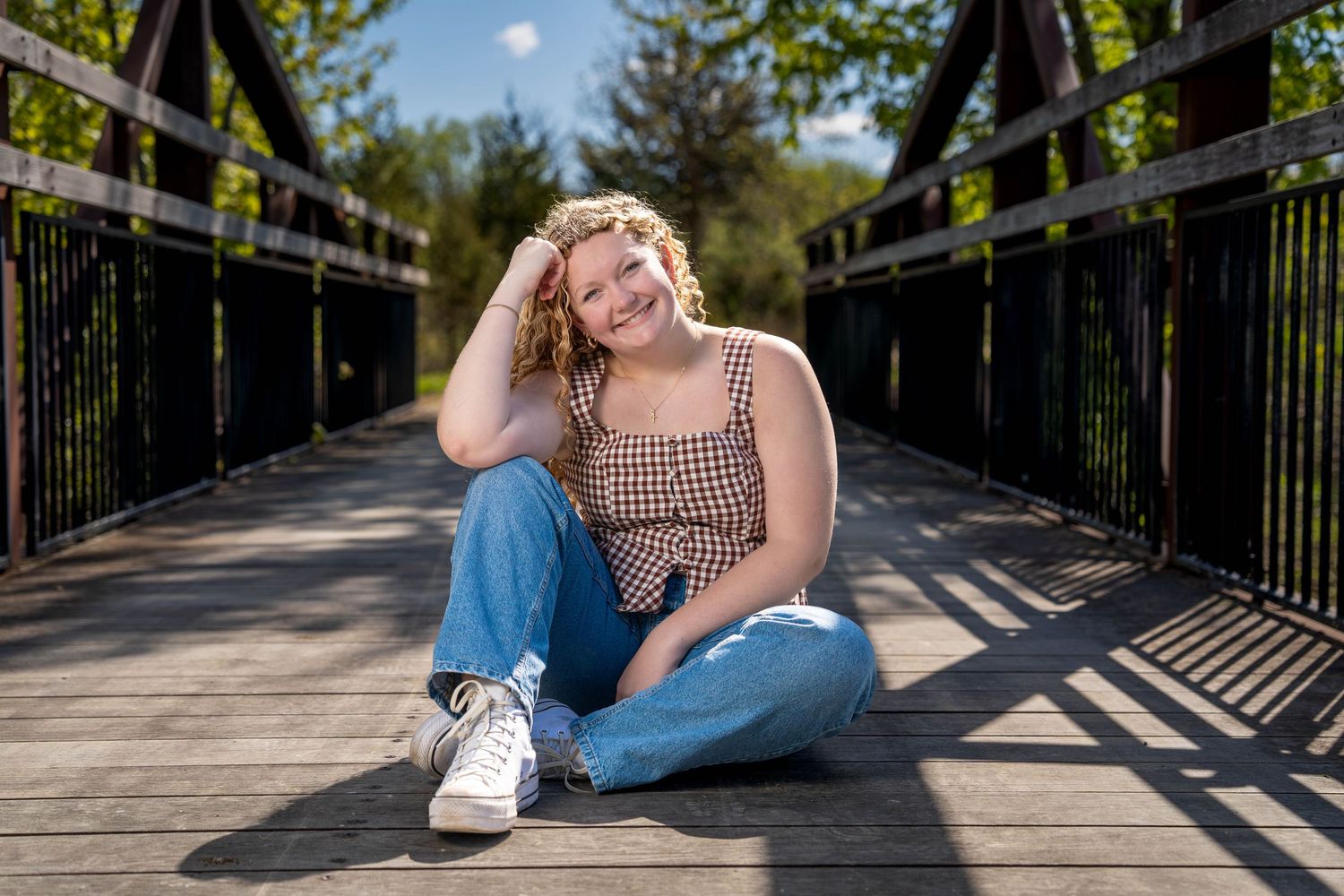 Relaxed senior portrait seated on a sunlit bridge