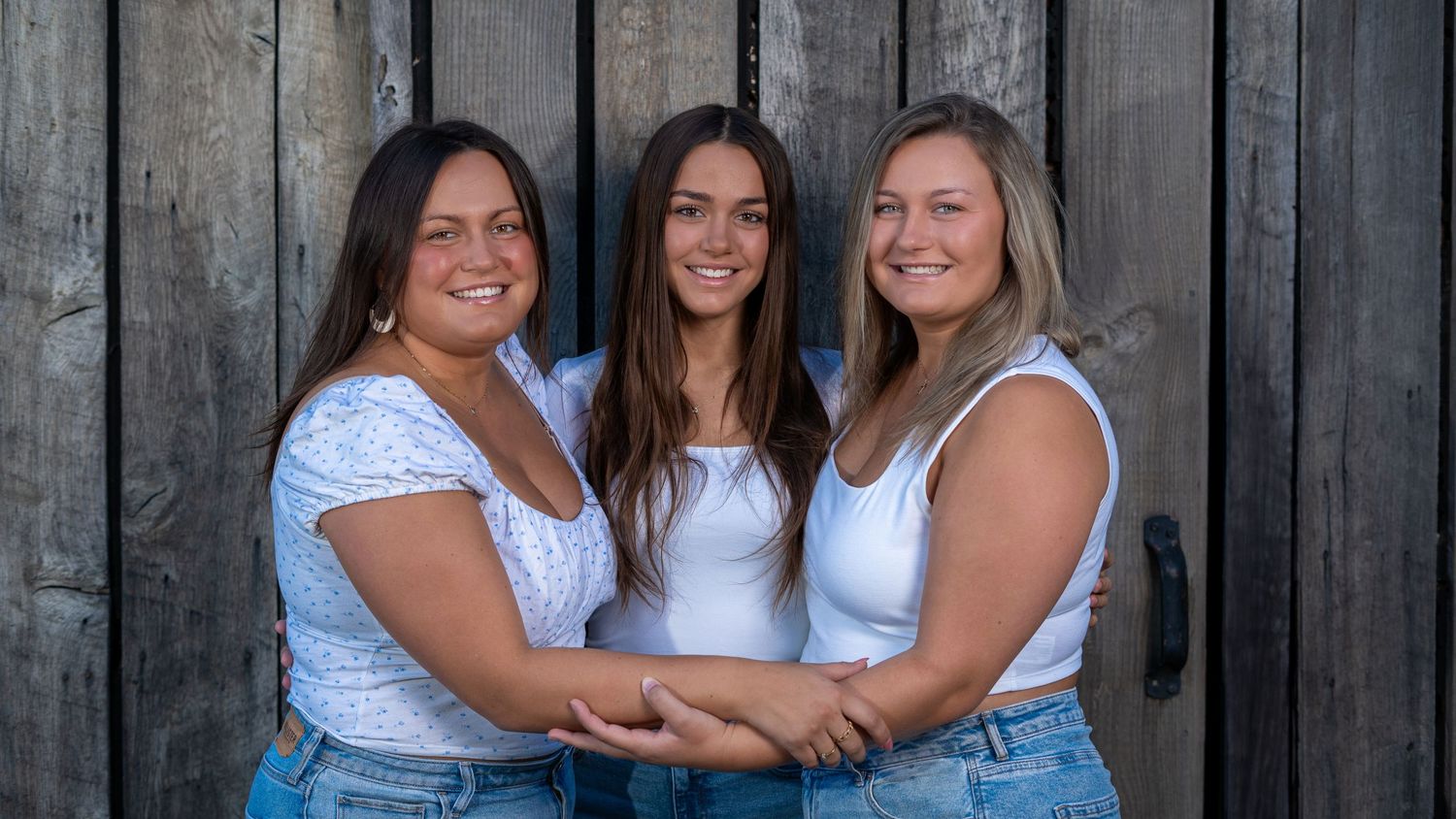 Three sisters embracing together against a rustic fence during a portrait session.