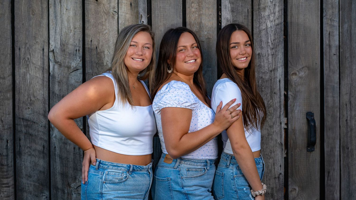 Three sisters standing together against a rustic fence during a portrait session.
