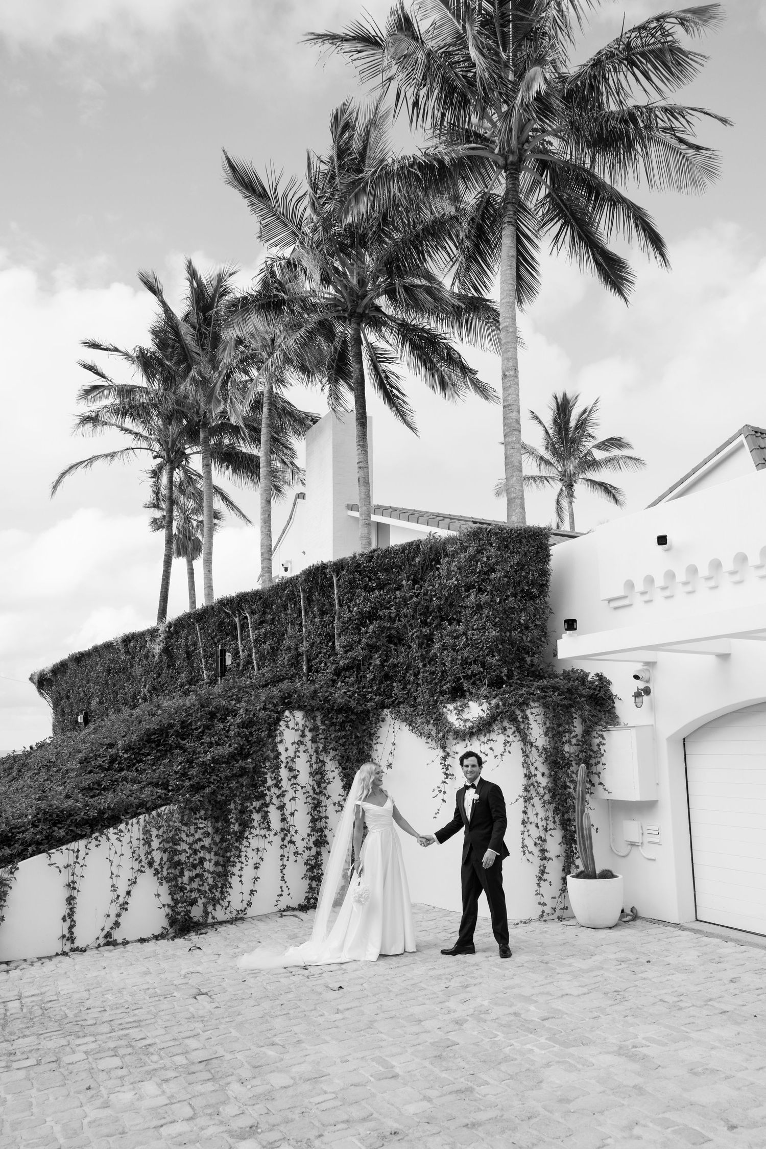 A series of black and white wedding photos showing a couple posing together on a beach with palm trees and white walls.
