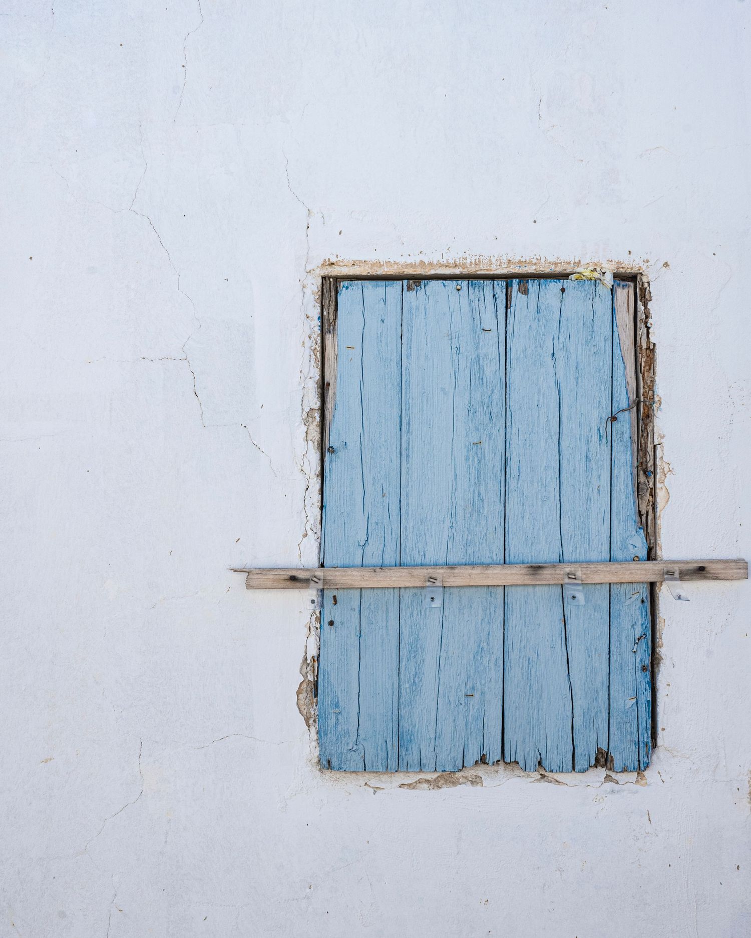Weathered blue wooden window shutters on a rustic white Mediterranean wall with peeling paint.