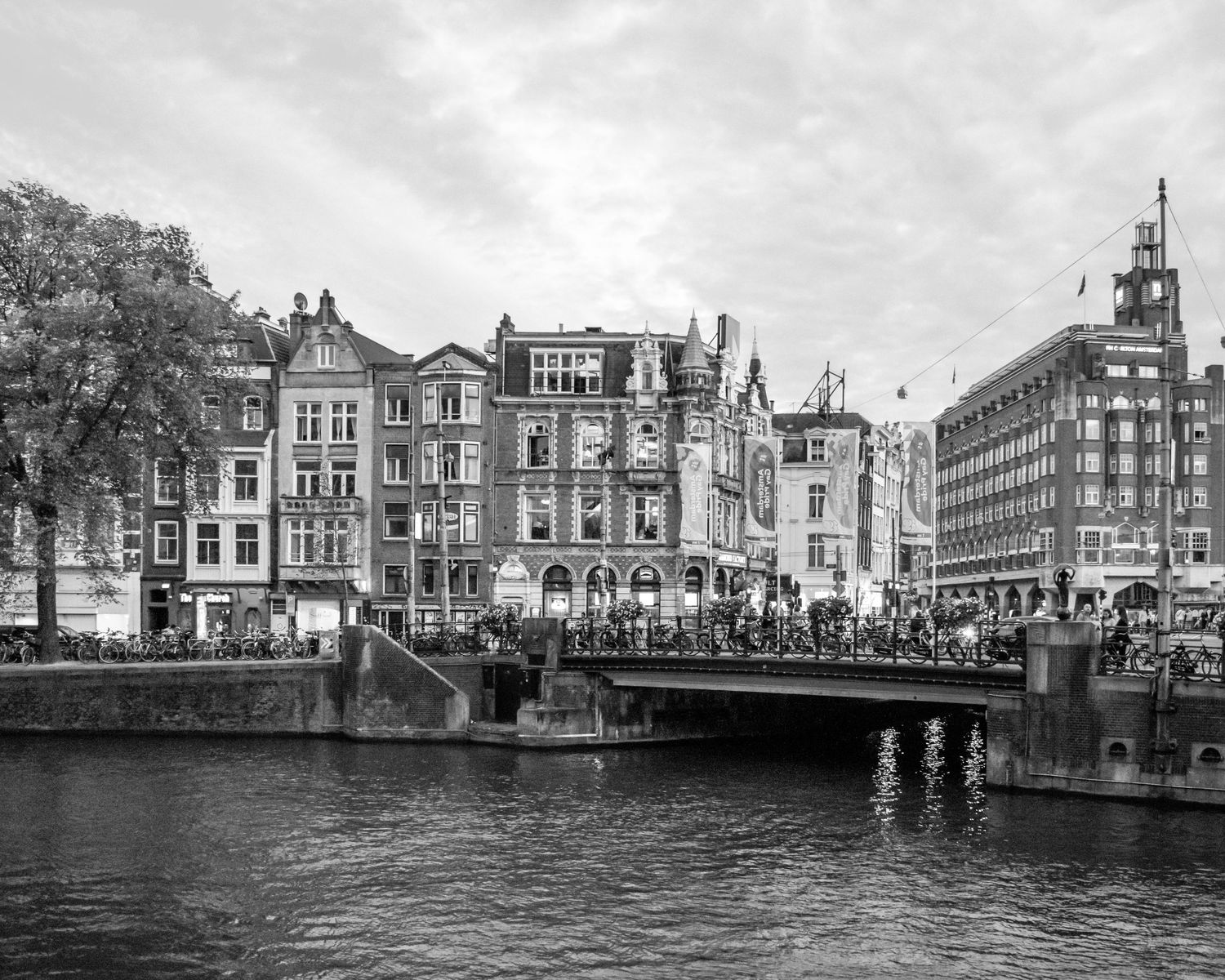 Black and white photo of a busy bridge over an Amsterdam canal with historic Dutch buildings in the background.