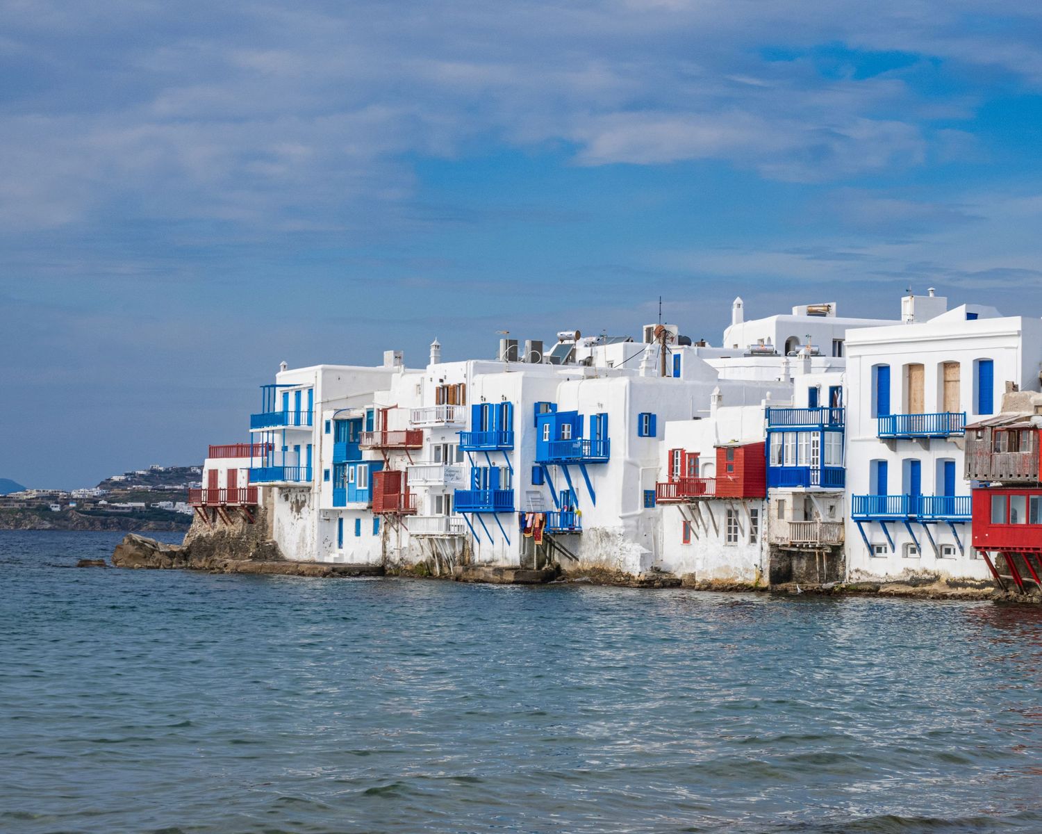 Colorful white and blue buildings of Little Venice in Mykonos, Greece, standing along the turquoise Aegean Sea.