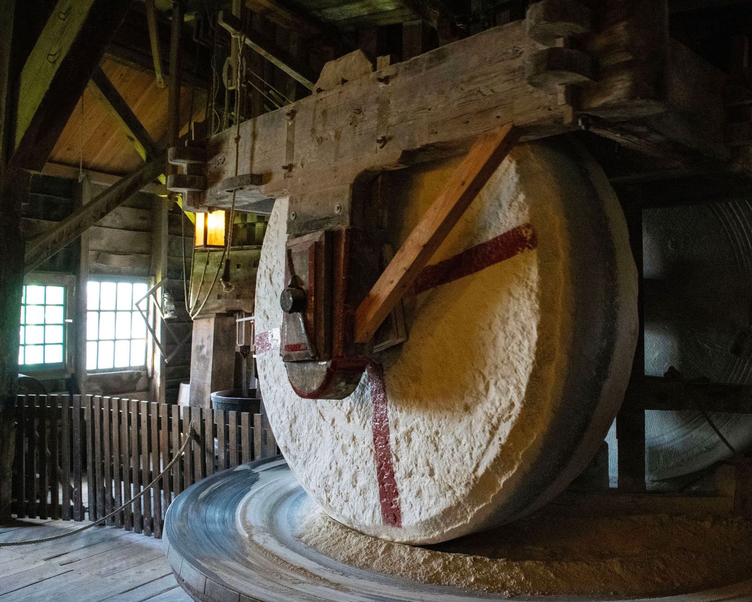 Large millstone grinding wheel inside a historic wooden grist mill with timber frame construction.