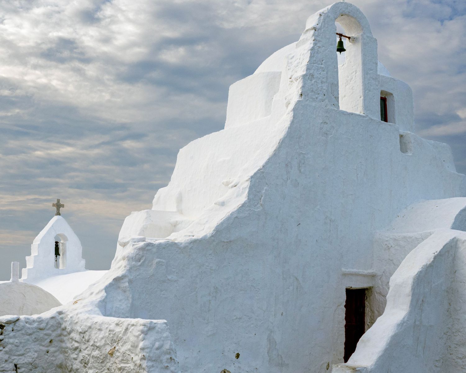 White-washed Greek Orthodox church with bell tower against cloudy sky in Mykonos, Greece.