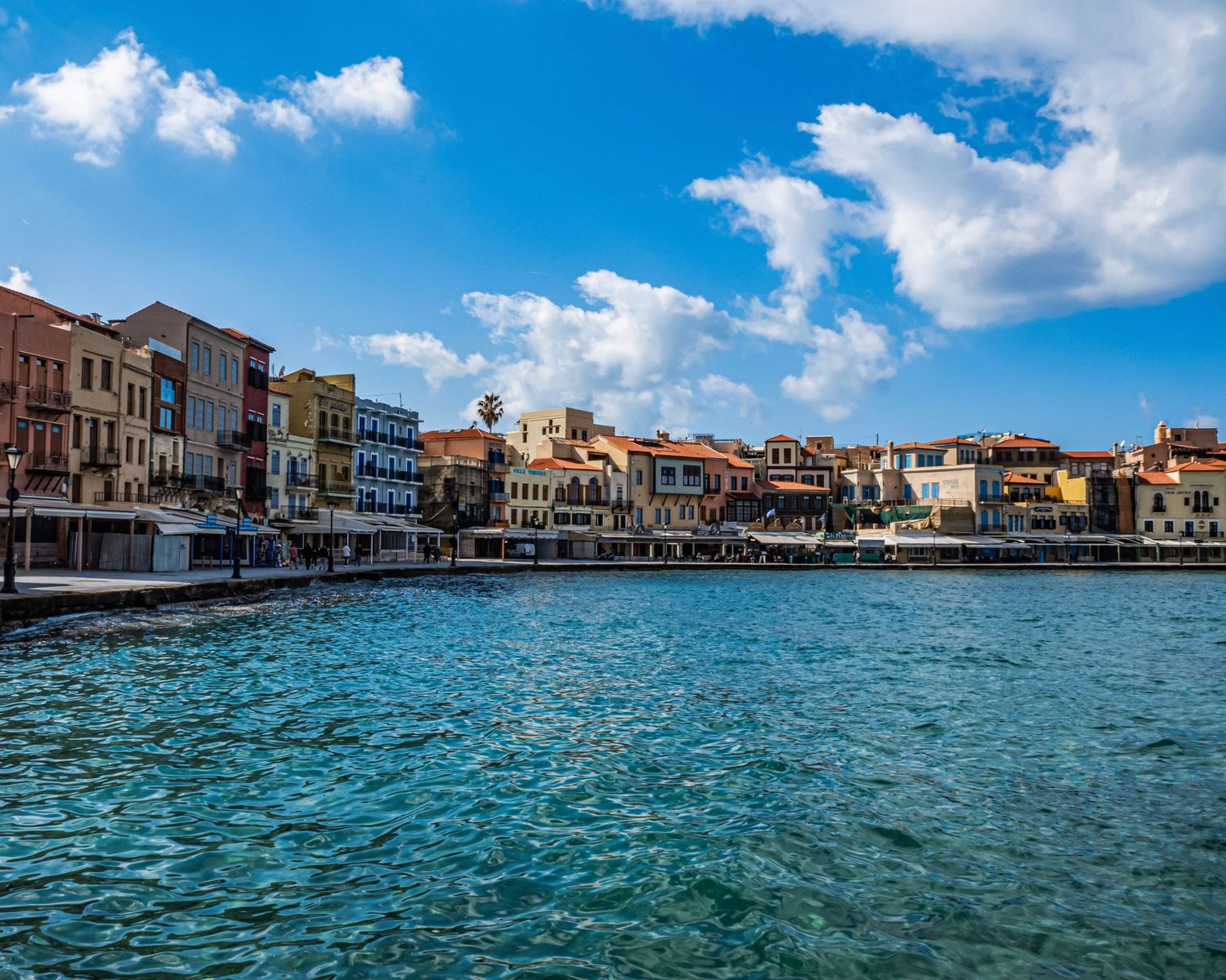 Colorful waterfront buildings line the picturesque harbor of Chania, Crete, reflecting in the crystal-clear turquoise waters.