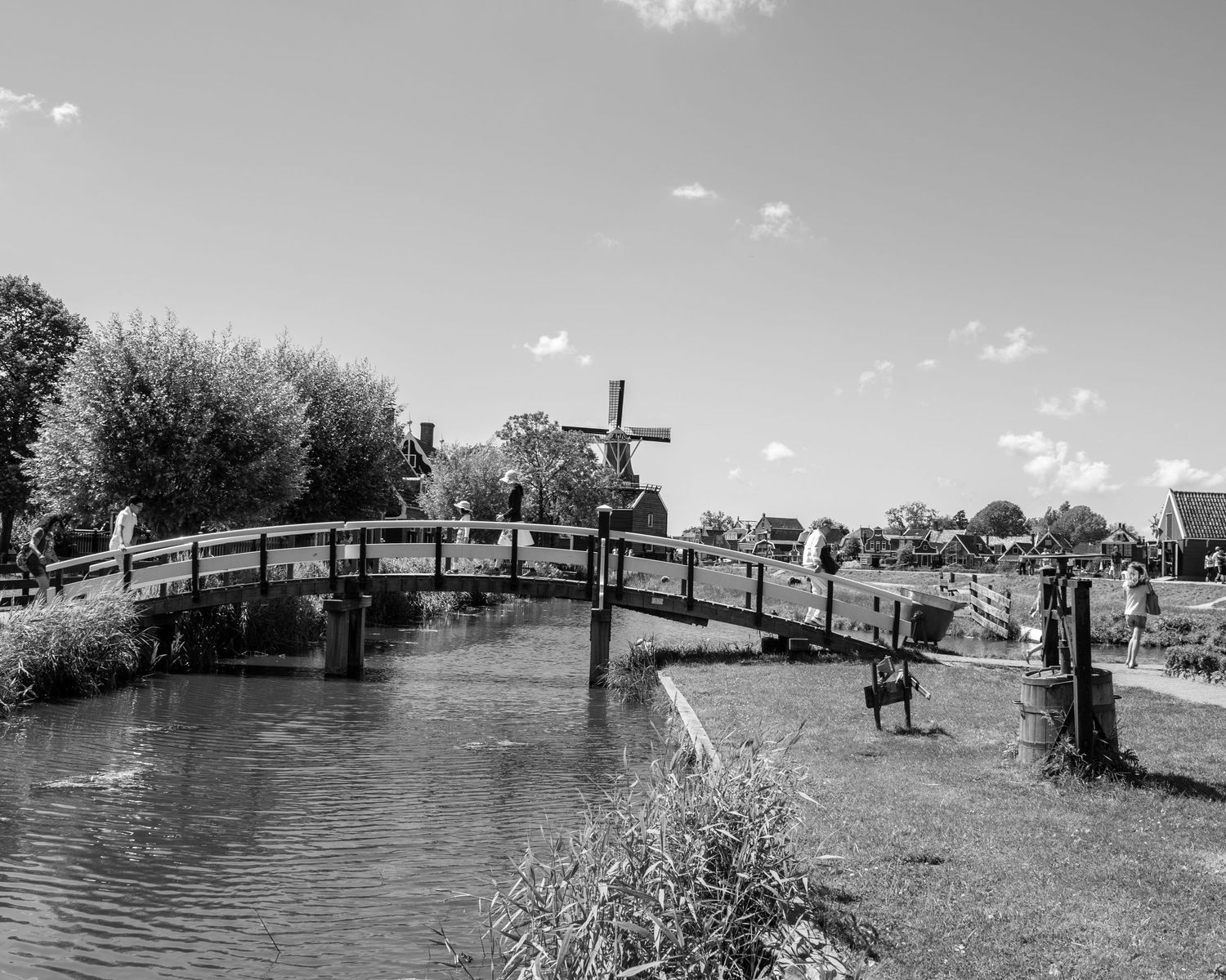 Black and white photo of a wooden arched bridge over a canal with a windmill in the background.
