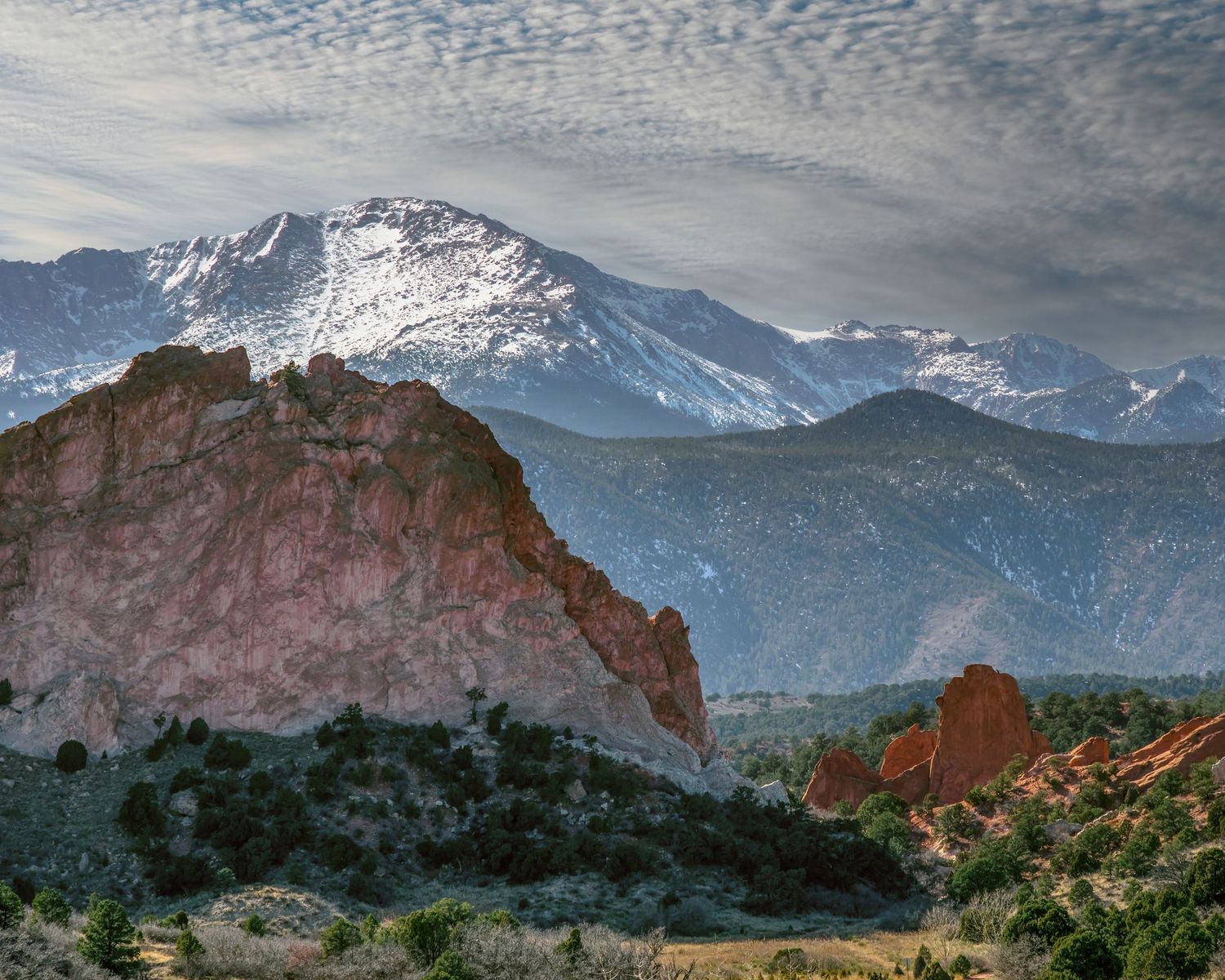 Red rock formations at Garden of the Gods with snow-capped Pikes Peak and dramatic cloudy sky in Colorado Springs.