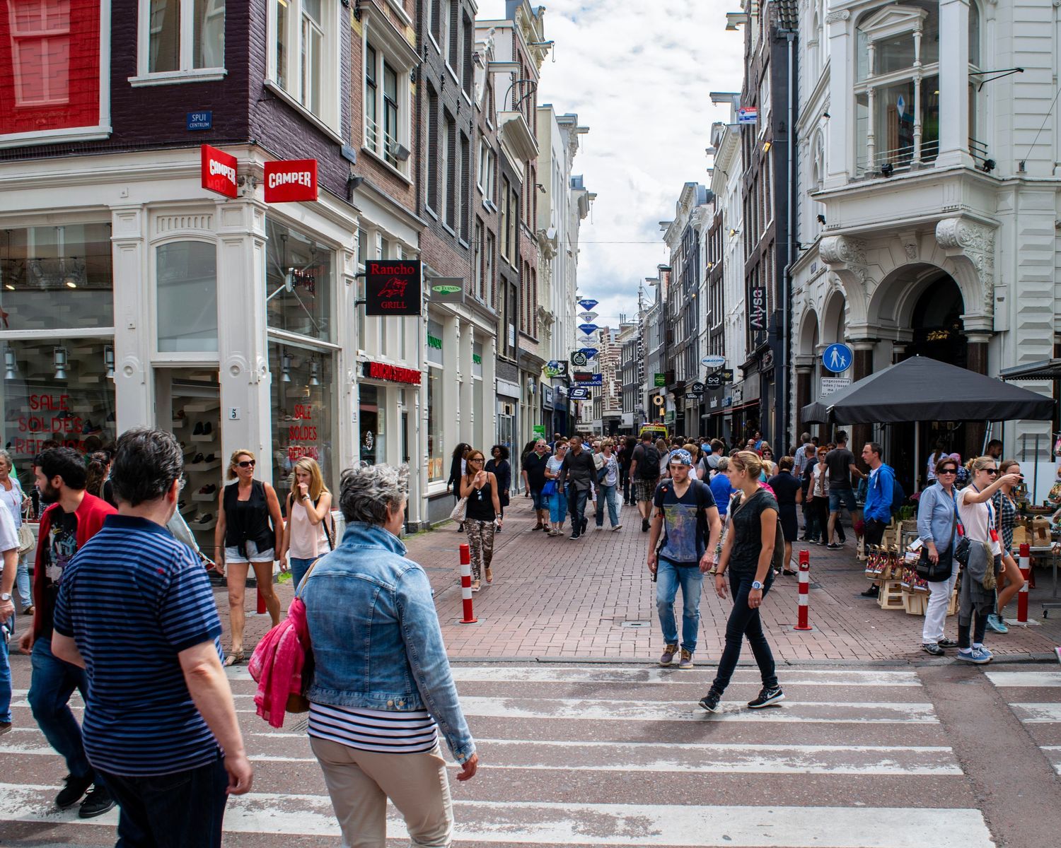 Busy pedestrian shopping street in Amsterdam with crowds of tourists walking past retail stores on a summer day.