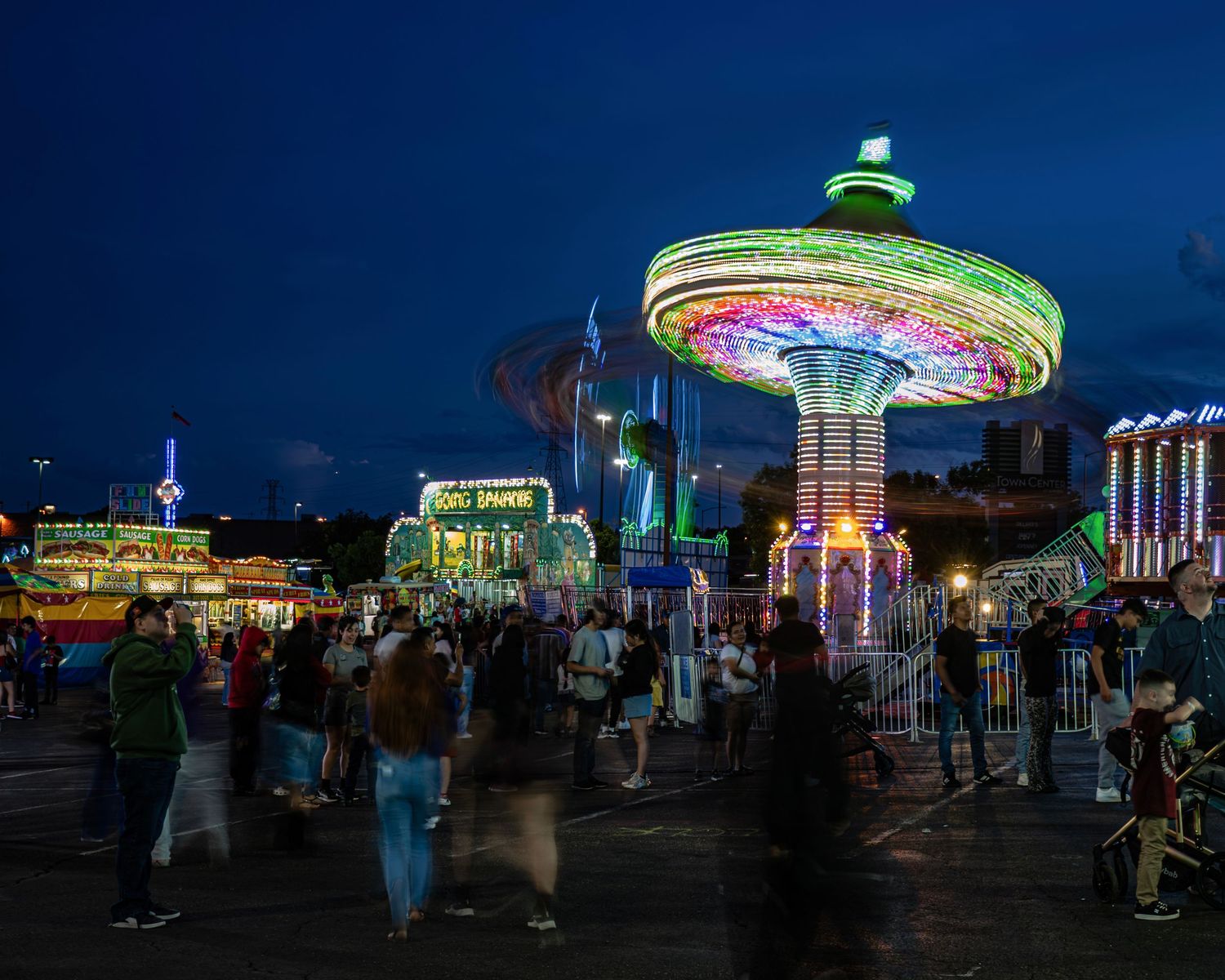 Colorful spinning carnival ride glows at night fair with crowds of people walking around illuminated amusement park attractions.