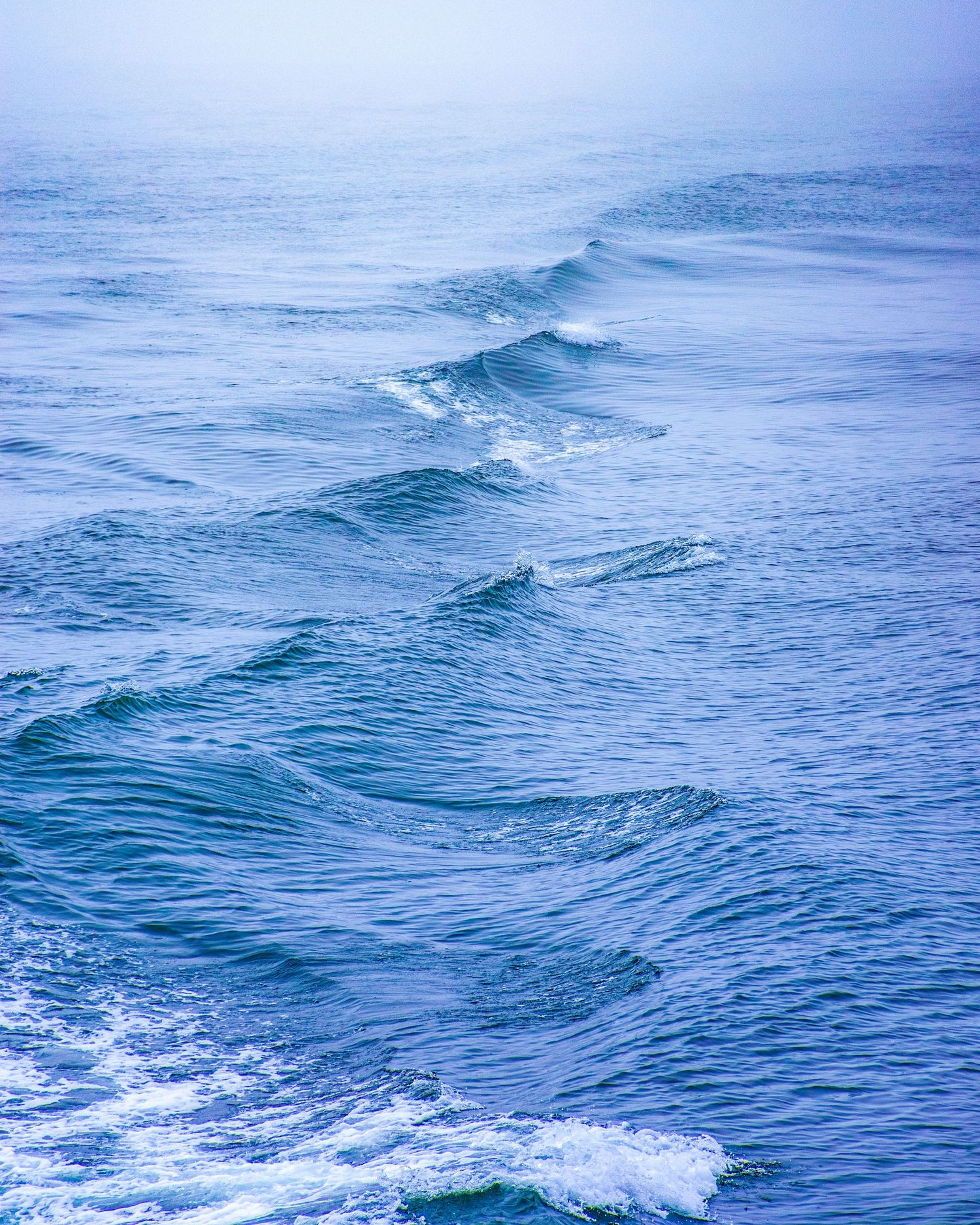 Blue ocean waves rolling in misty sea water, creating a serene and tranquil seascape with gentle whitecaps.