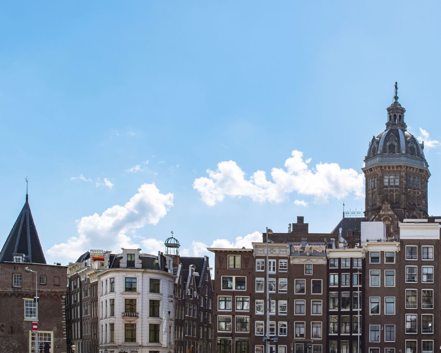 Historic Amsterdam canal houses with stepped gable facades beneath a blue sky, featuring a prominent church tower in the background.