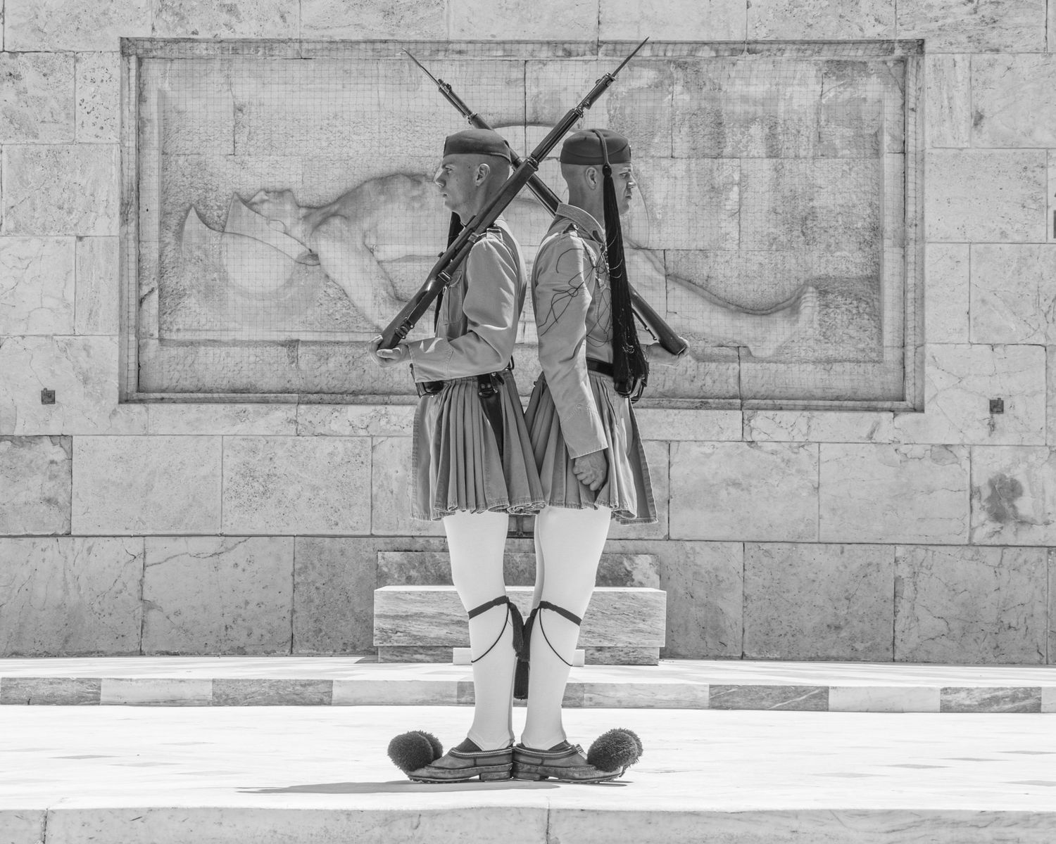Two Evzone guards in traditional Greek uniforms stand at attention with crossed rifles at the Tomb of the Unknown Soldier.