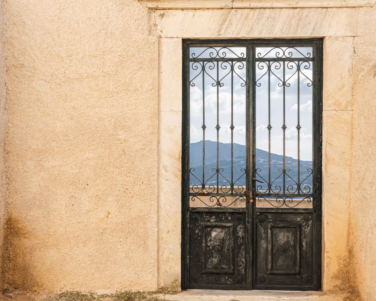 Black ornate wrought iron double doors set in a weathered stone wall with mountain views visible through the decorative grille.