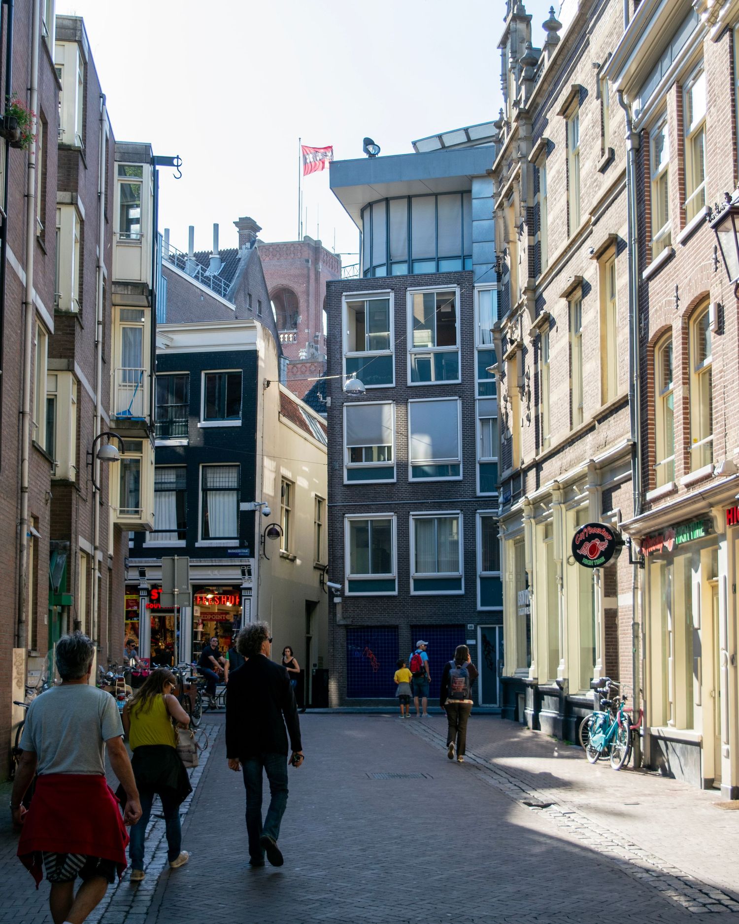 Pedestrians walking through a narrow cobblestone street lined with historic Dutch buildings in Amsterdam.