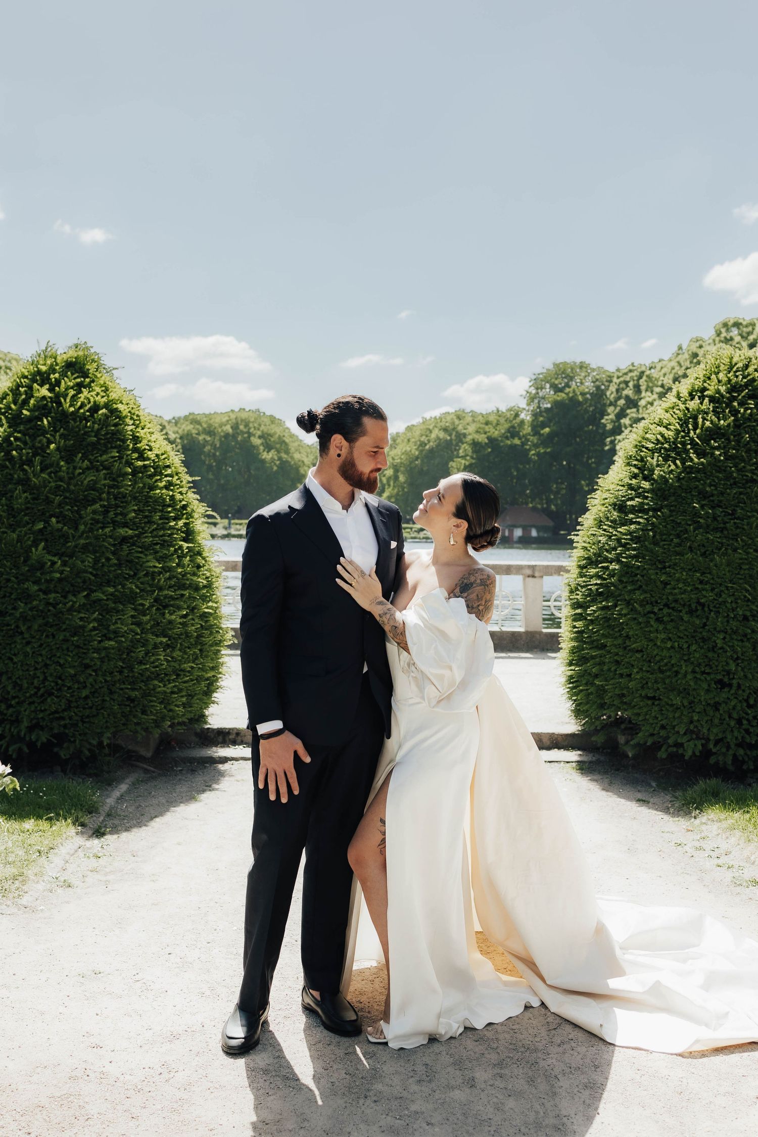 A couple in wedding attire shares romantic moments between manicured hedges in a garden setting.