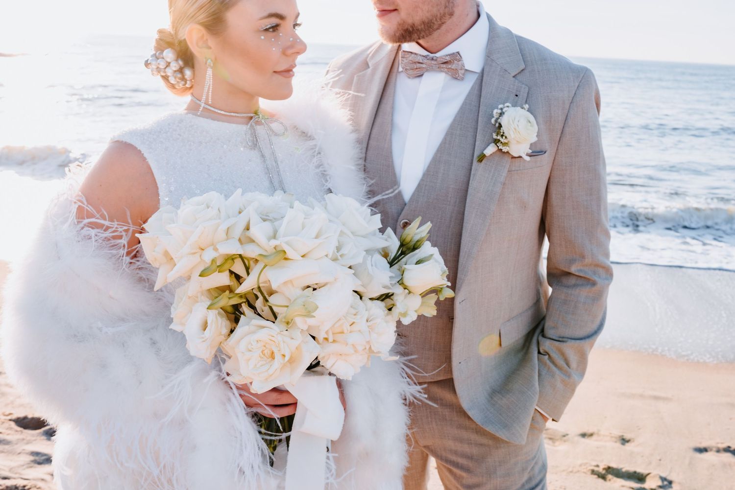 Elegant coastal wedding couple holding a luxurious white bouquet on a sunny beach.