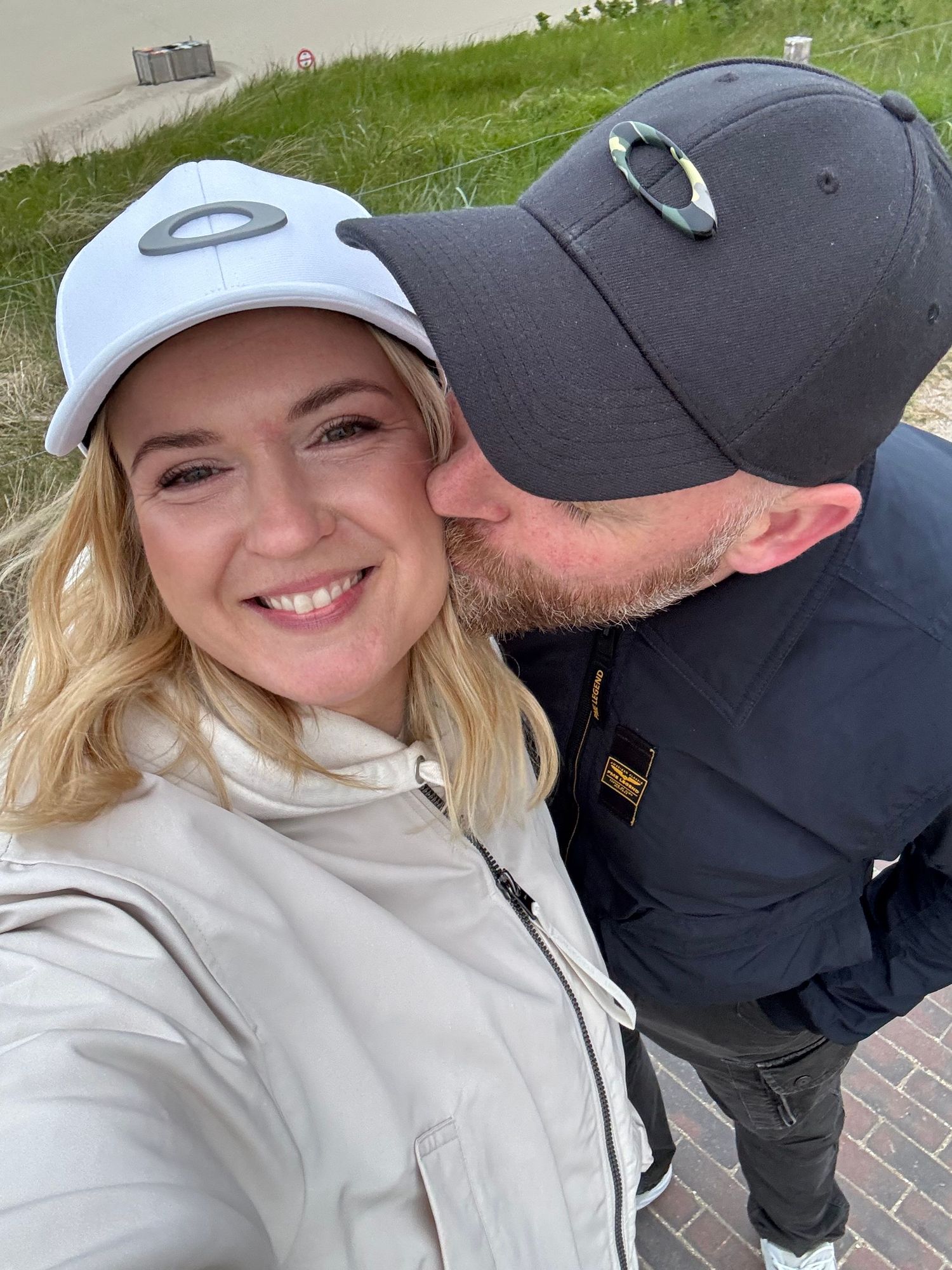 A selfie of two people wearing baseball caps outdoors on a sunny day.